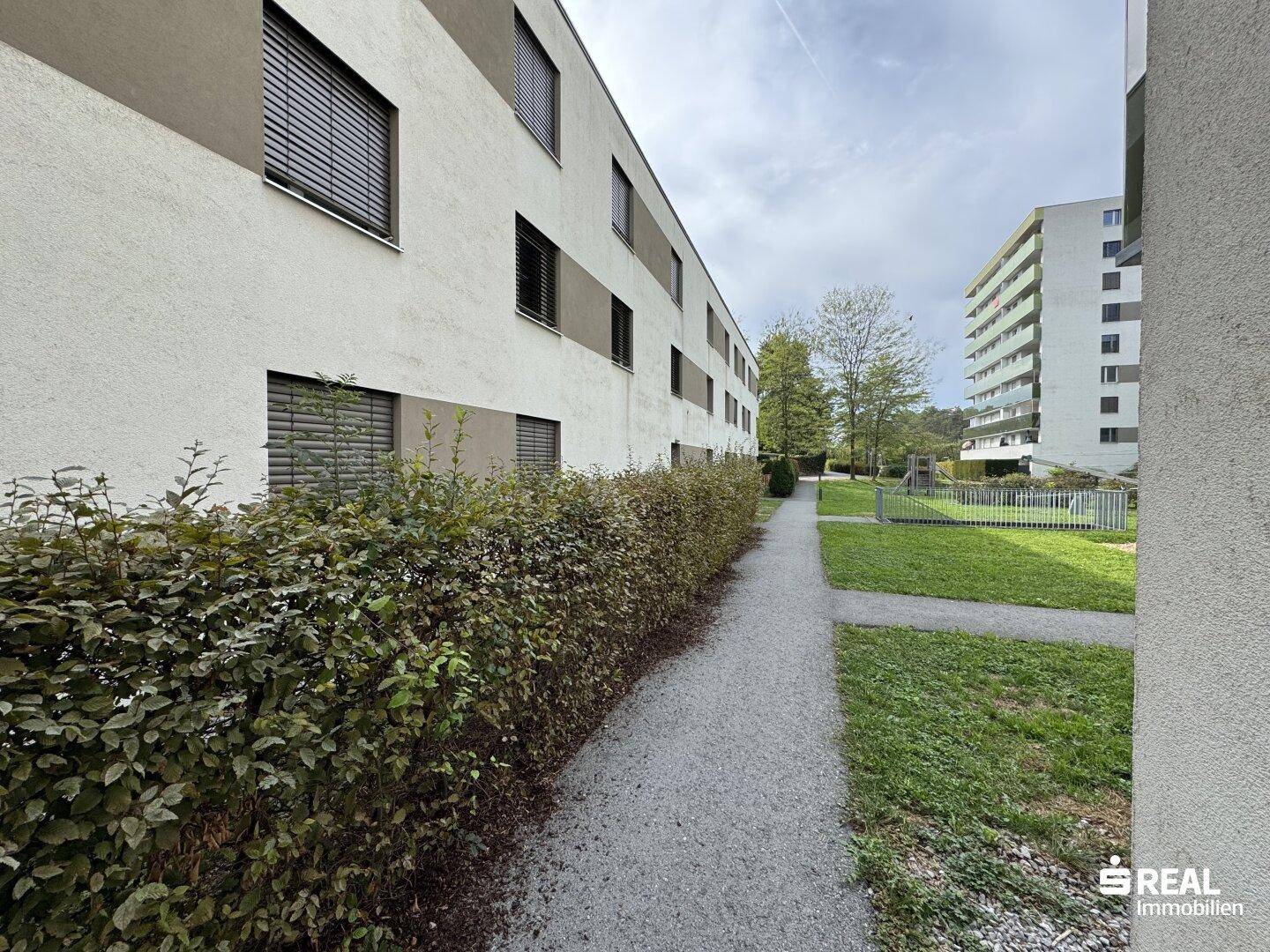 Wohnanlage mit gepflegten Grünflächen und Wegen, umgeben von Bäumen und Hecken.