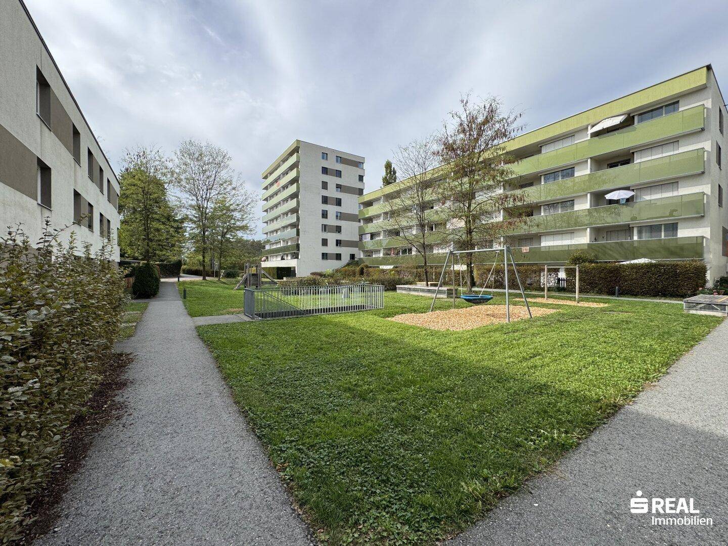 Gemeinschaftsgarten mit Spielplatz und Grünflächen zwischen modernen Wohngebäuden.