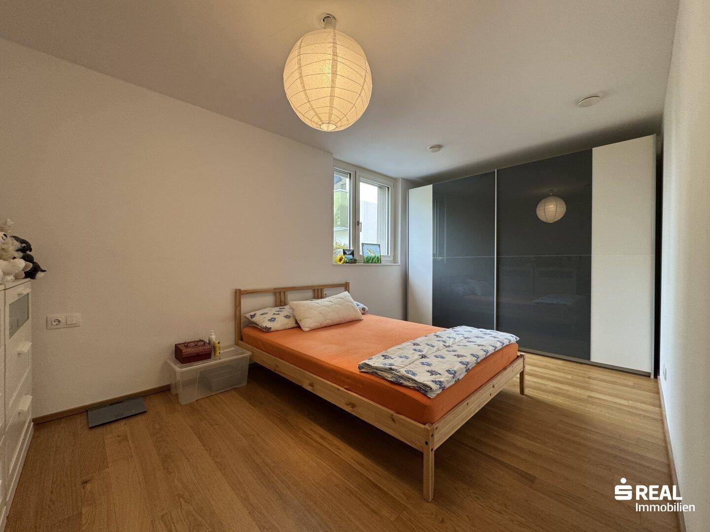 Helles Schlafzimmer mit Holzboden, großem Kleiderschrank und Fenster mit Grünblick.