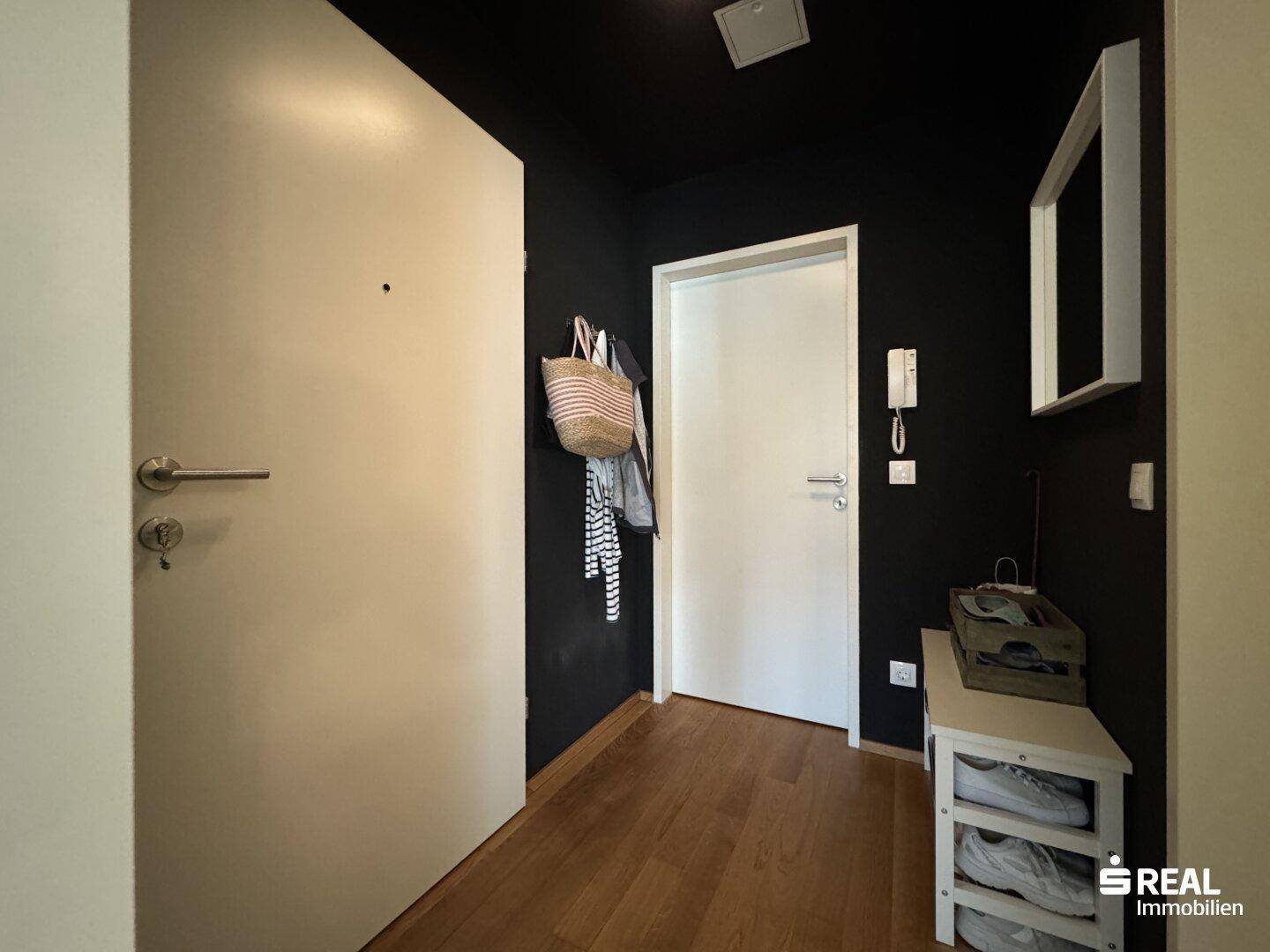 Moderner Eingangsbereich mit dunkler Akzentwand und Holzboden, bietet Platz für Garderobe.