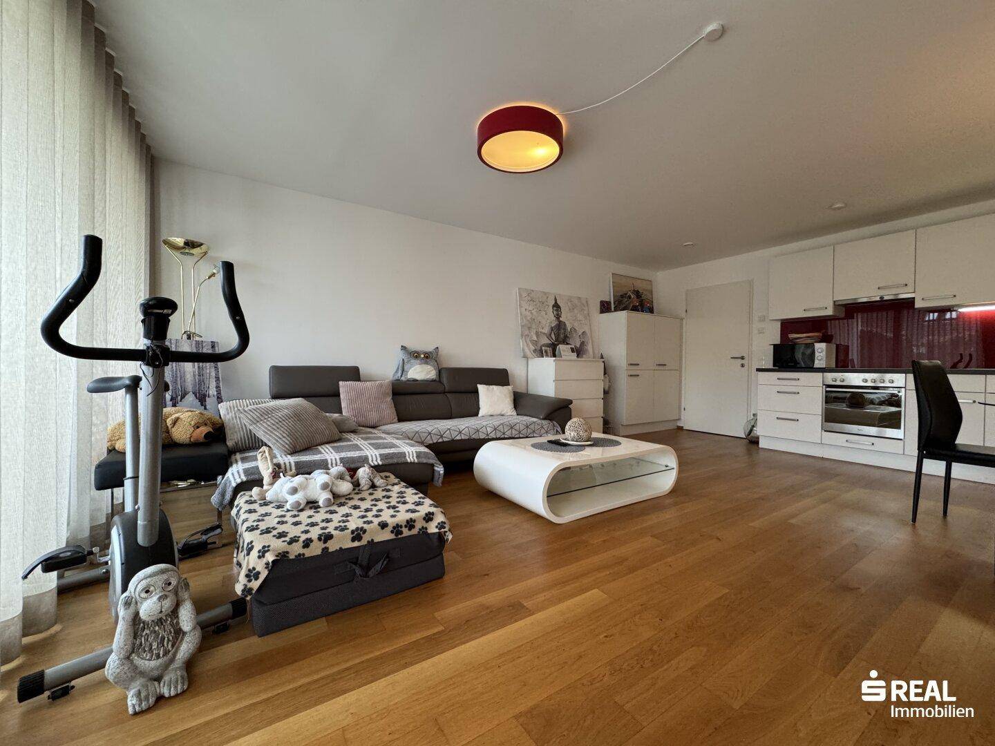 Offener Wohnbereich mit Holzboden, Sofa und Fitnessgerät, verbunden mit der Küche.