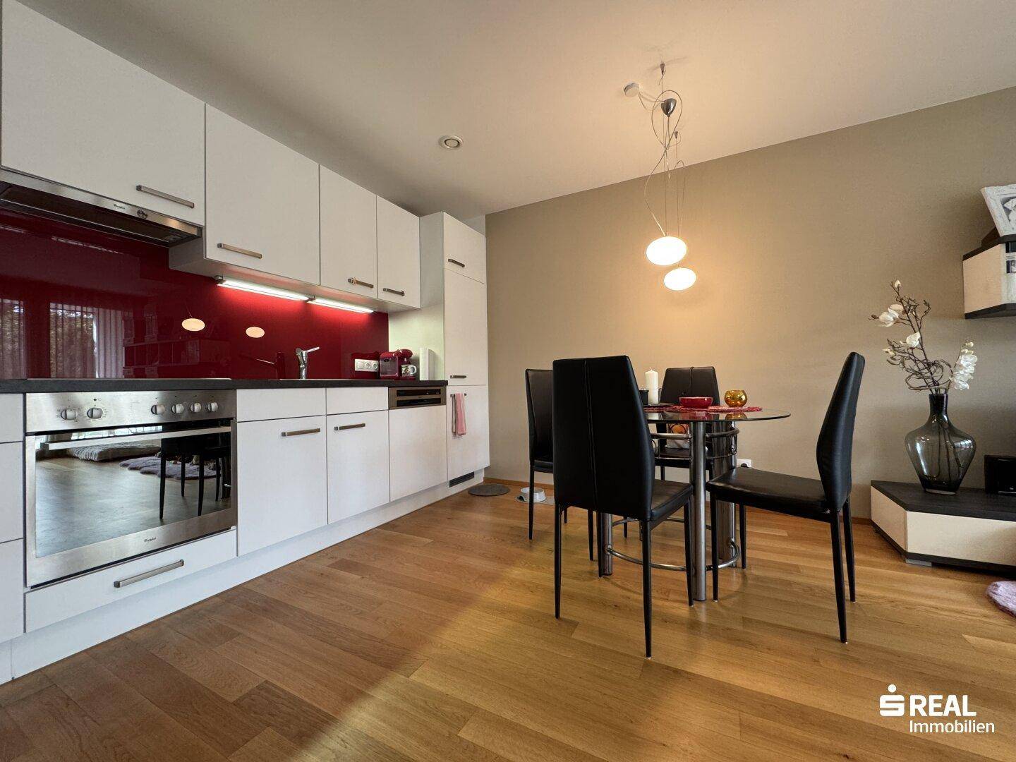 Moderne Einbauküche mit weißen Schränken, roter Rückwand und Essbereich.