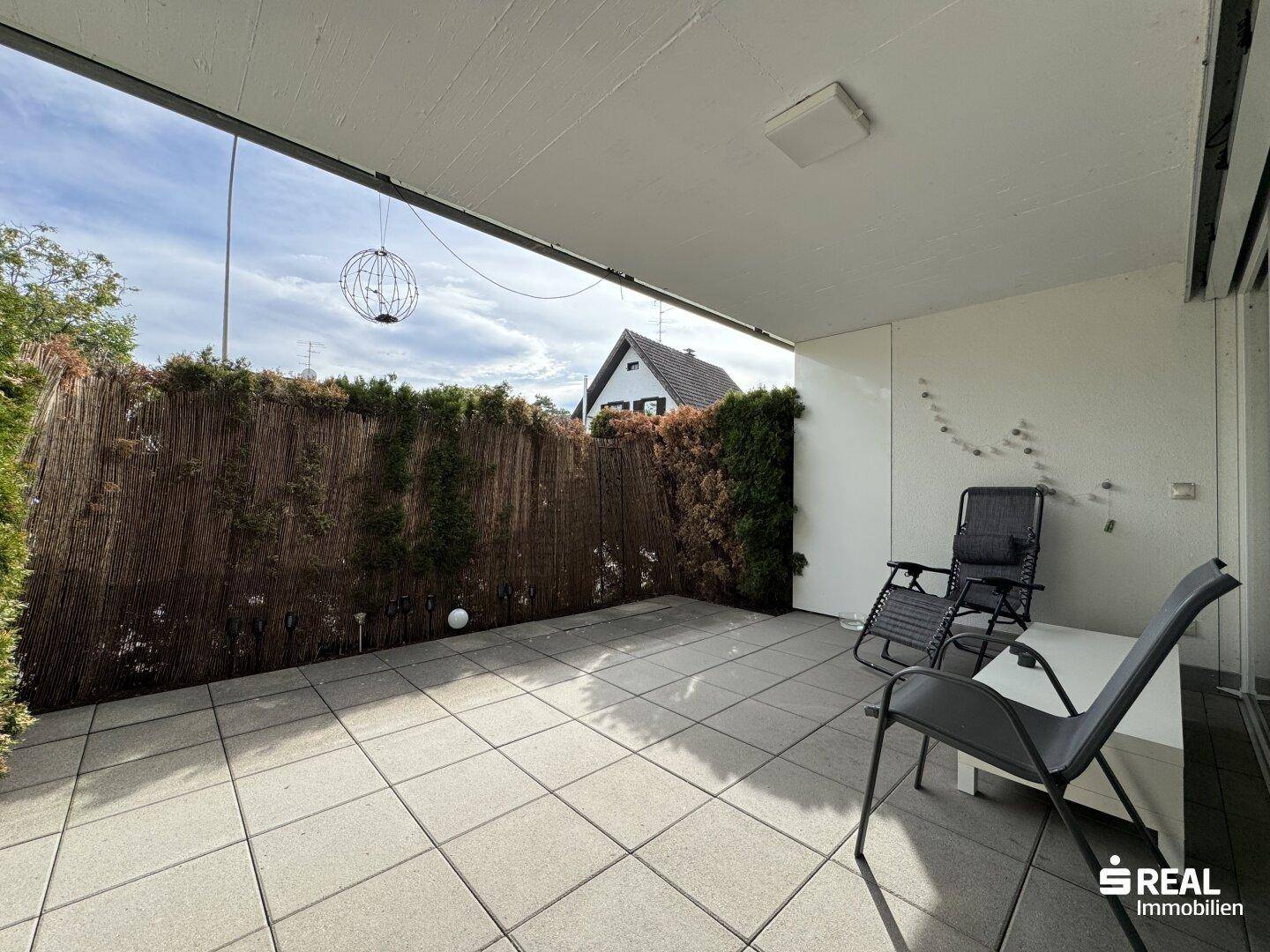 Überdachte Terrasse mit Fliesenboden und Sichtschutz, ideal für entspannte Stunden im Freien.
