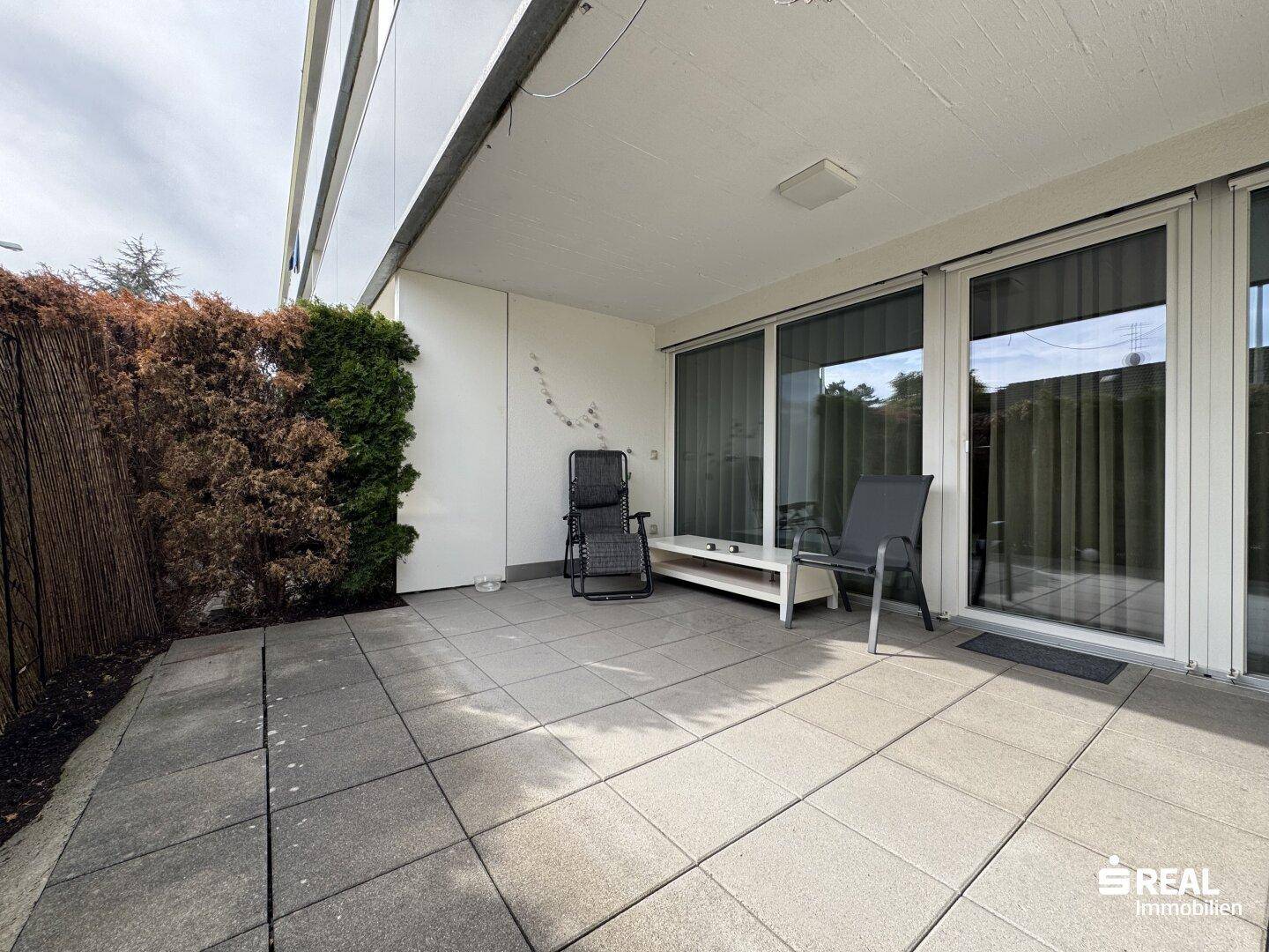 Große, geflieste Terrasse mit Schiebetüren und Blick ins Grüne, ideal für Entspannung.
