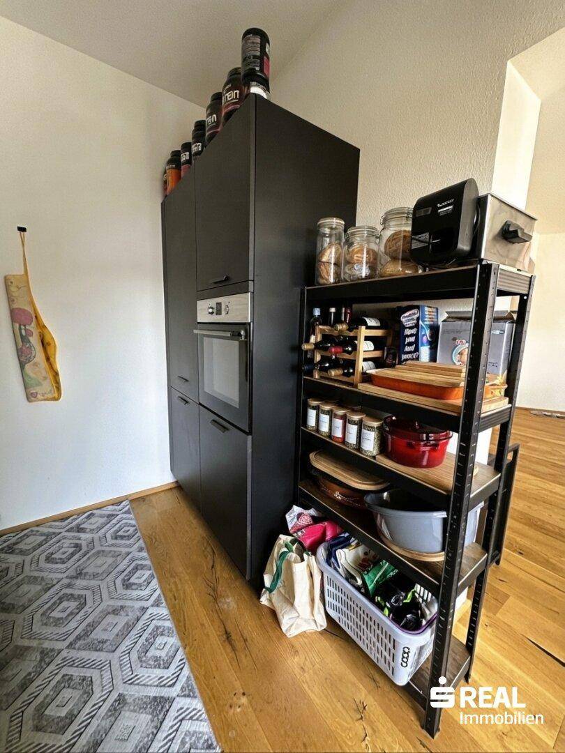 Küchenbereich mit hohem Schrank, integriertem Backofen und offenem Regal für Vorräte.