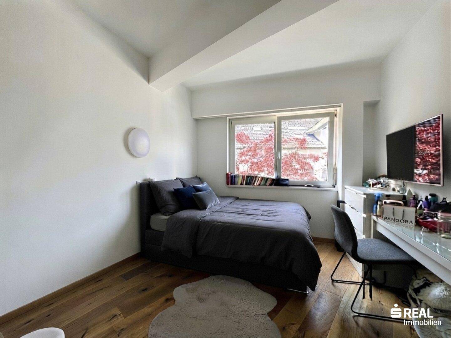 Schlafzimmer mit Holzboden, Doppelbett und Schreibtisch unter dem Fenster.