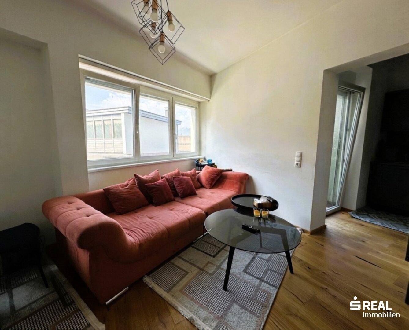 Gemütlicher Wohnbereich mit großem Sofa, Couchtisch und Blick nach draußen durch die Fenster.