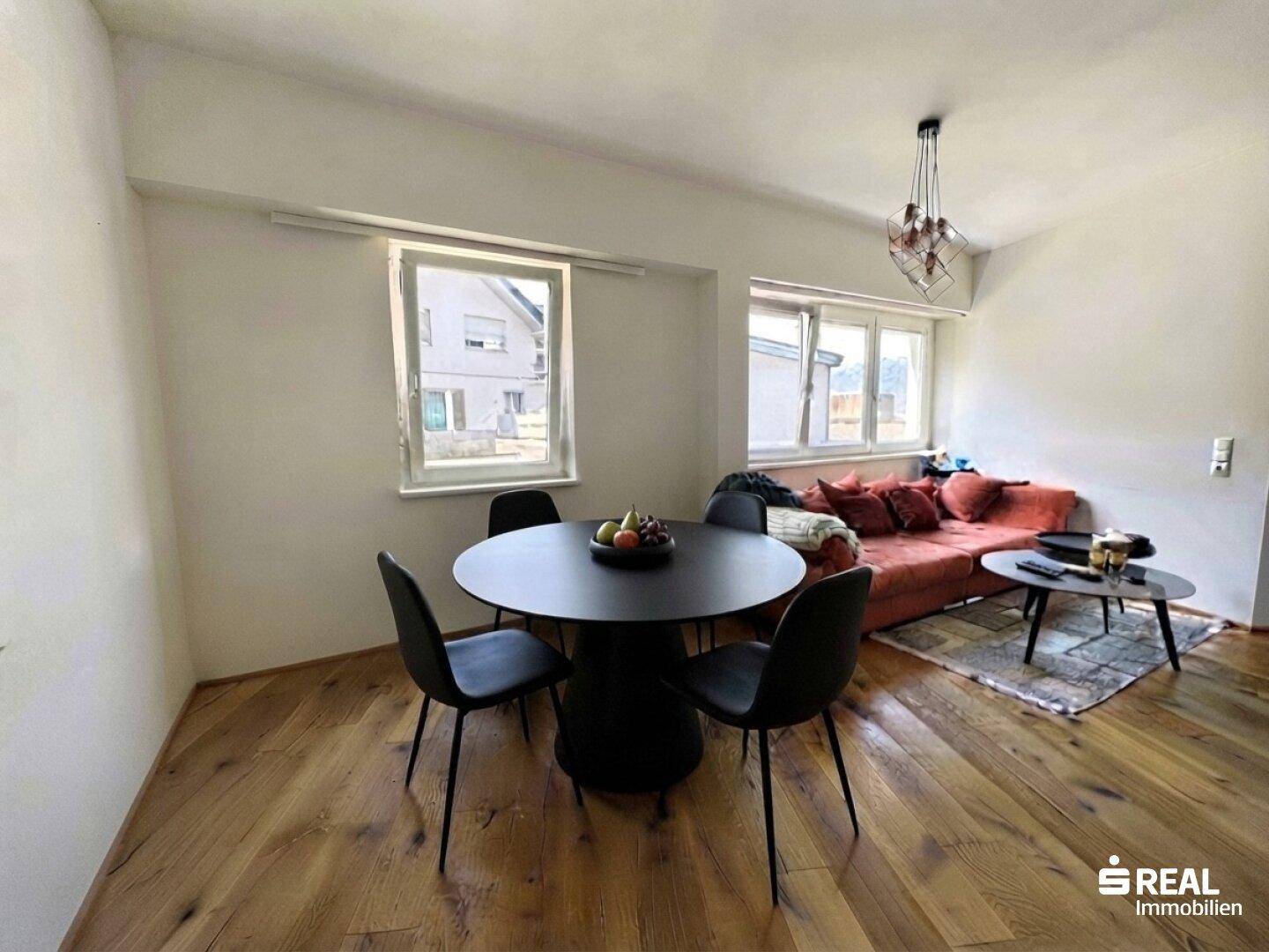 Heller Wohn-Essbereich mit Holzboden, Esstisch und gemütlichem Sofa am Fenster.