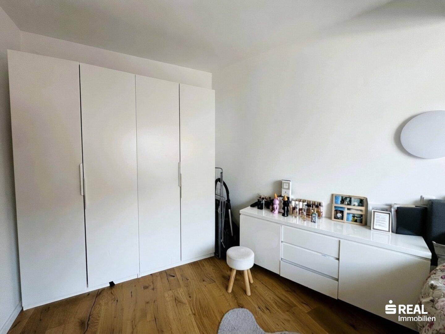 Schlafzimmer mit weißen Einbauschränken, Kommode und Holzboden.