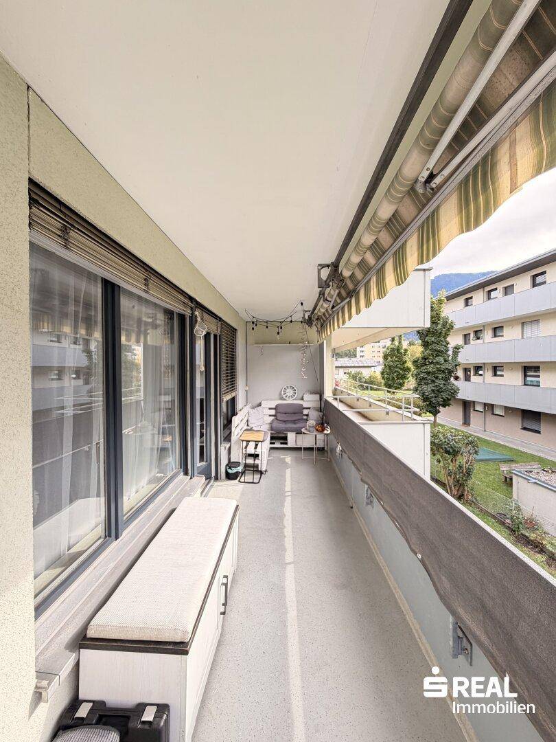 Langer Balkon mit Sitzgelegenheiten, Markise und Blick auf die umliegenden Gebäude.