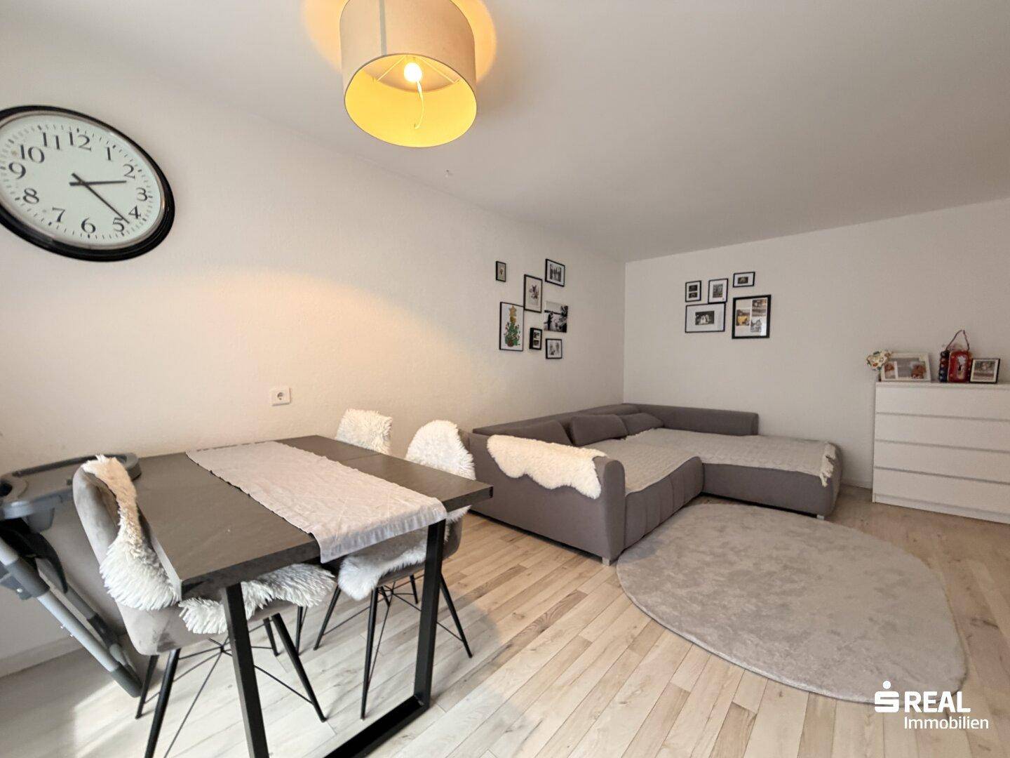 Gemütlicher Wohn-Essbereich mit großem Sofa, Esstisch und heller Wandgestaltung.