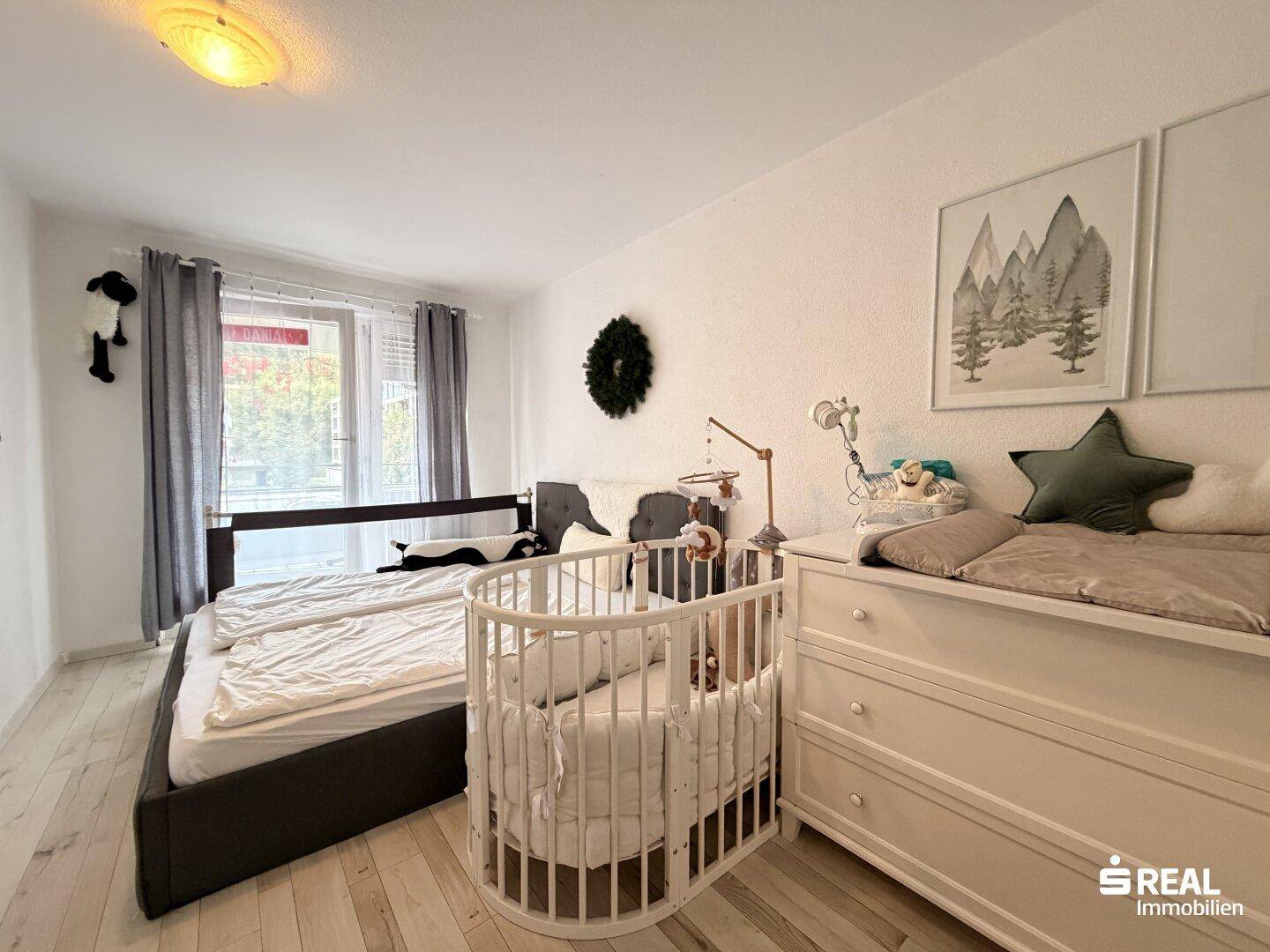 Helles Schlafzimmer mit Doppelbett, Babybett und hellem Laminatboden.