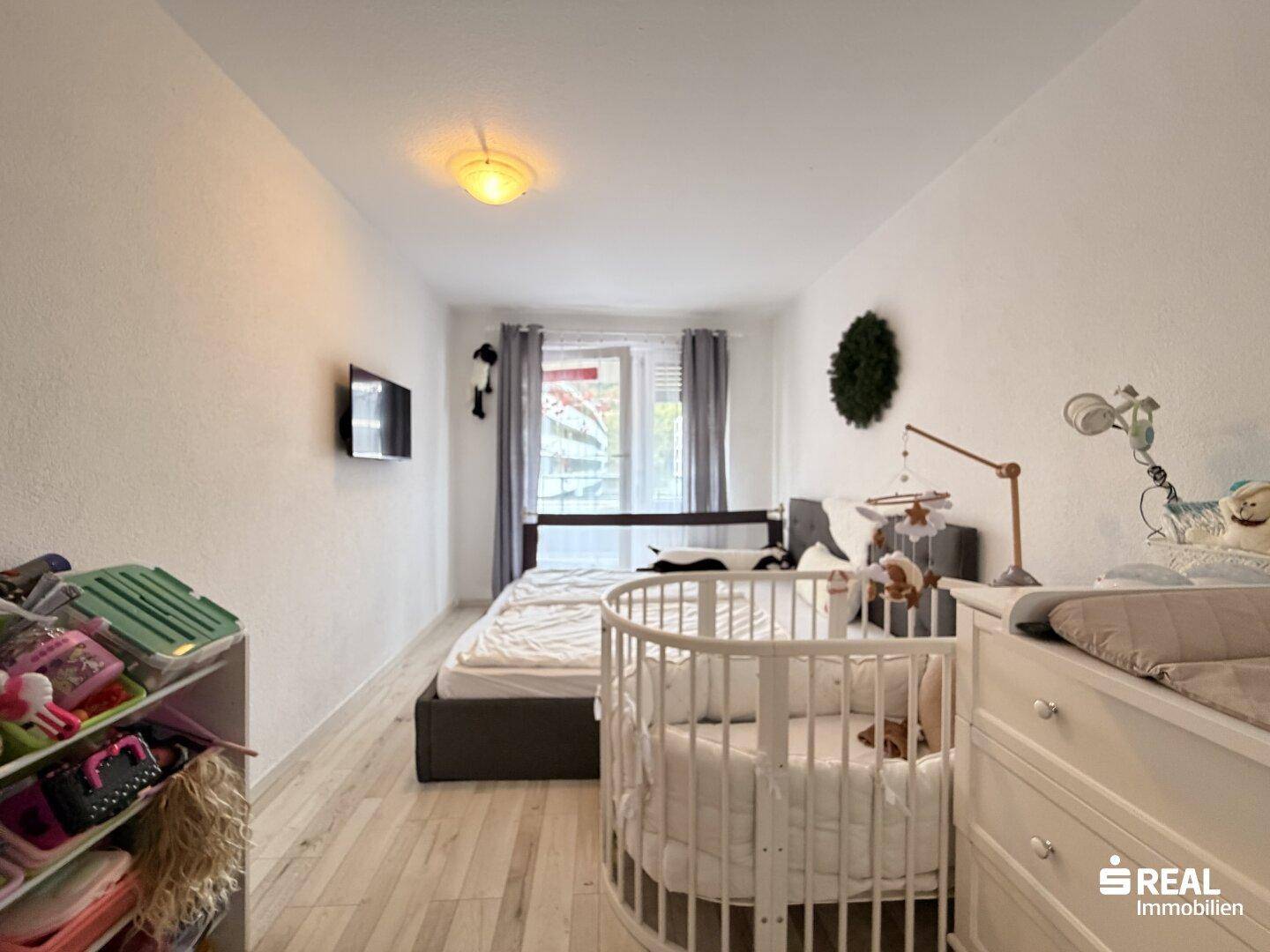 Geräumiges Schlafzimmer mit Doppelbett, Babybett und Fernseher an der Wand.