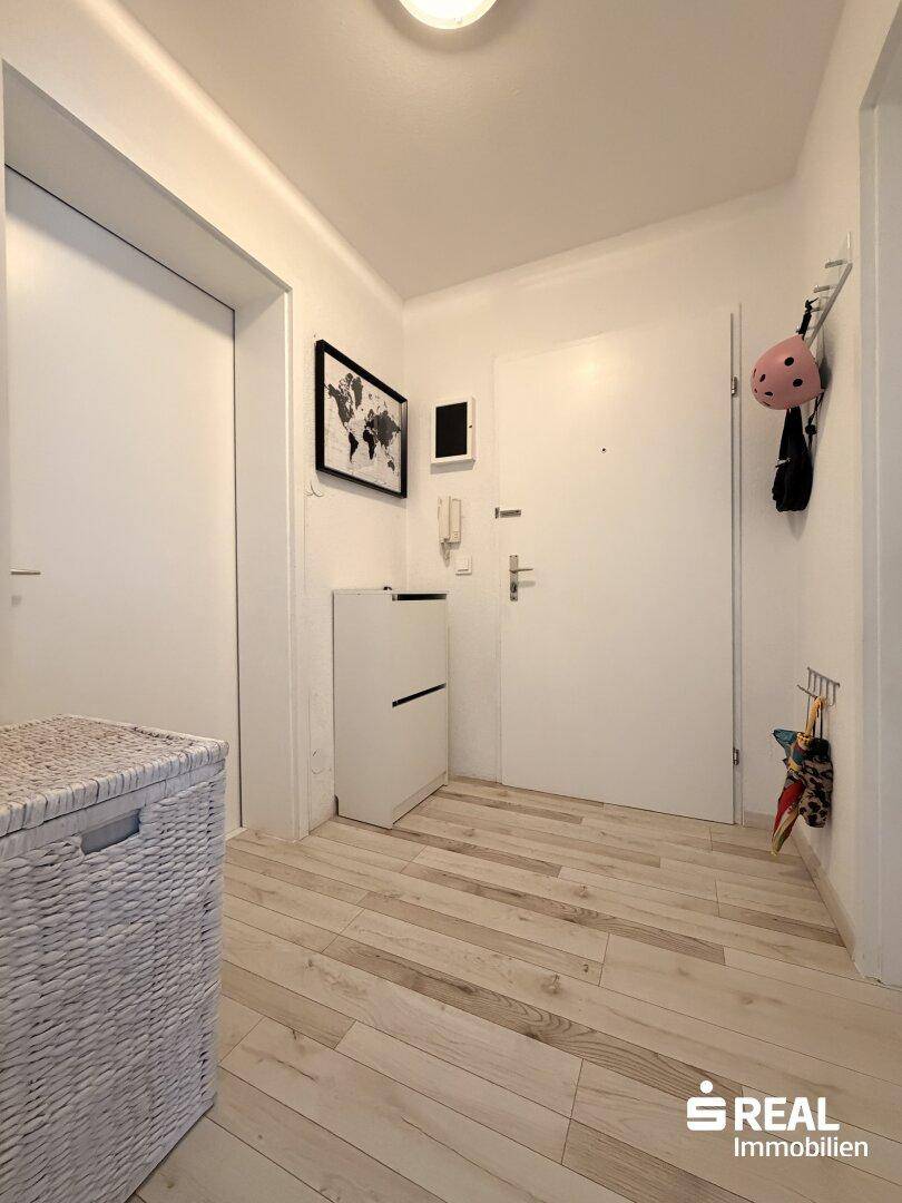Heller Flur mit Holzboden, weiß gestrichenen Wänden und Schuhschrank.