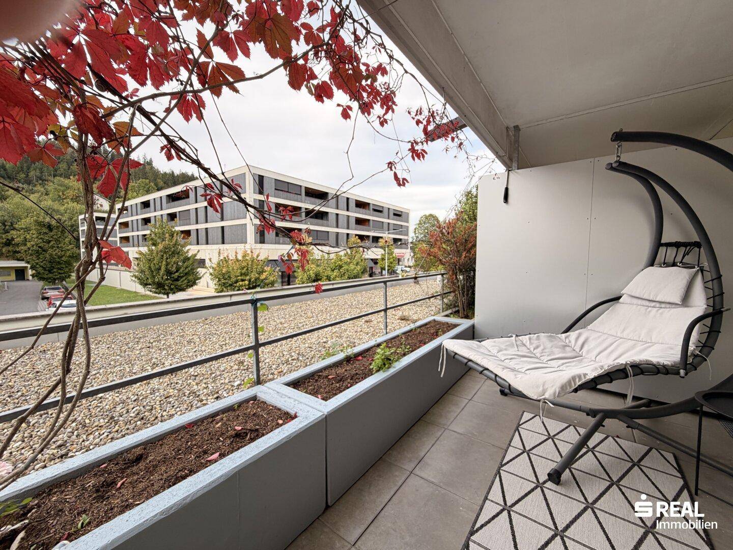 Balkon mit Hängesessel und Pflanzen, bietet einen Ausblick auf moderne Architektur.