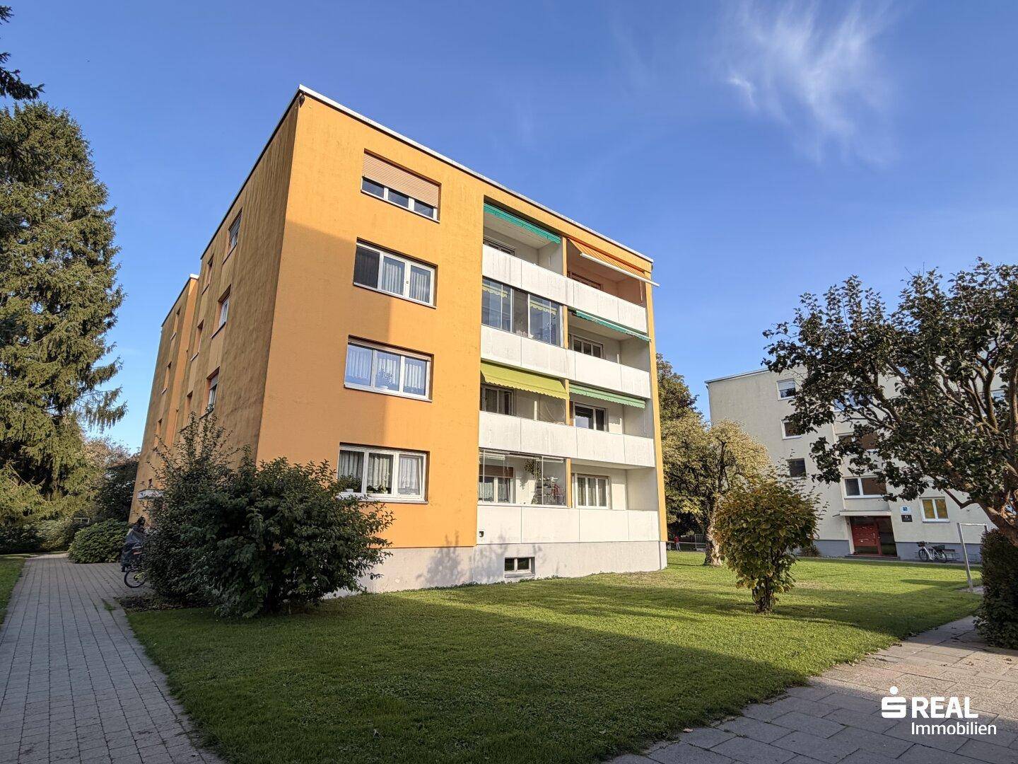 Mehrfamilienhaus mit gelber Fassade, Balkonen und gepflegter Grünanlage.
