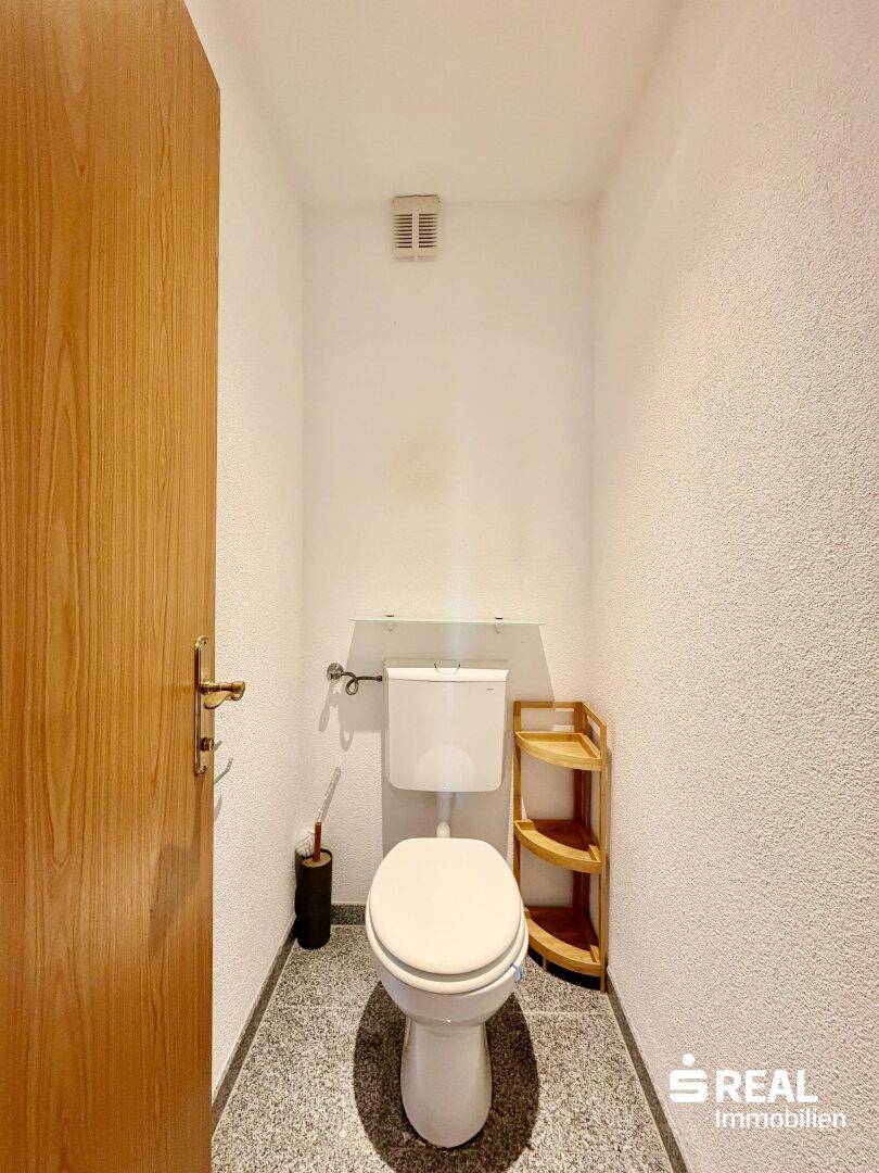 Kleines Gäste-WC mit Toilette, Fliesenboden und einfacher Einrichtung.