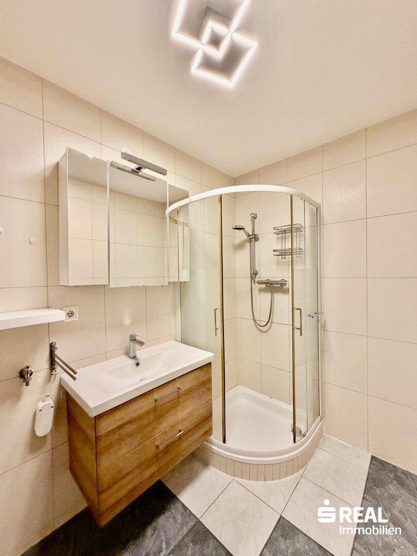 Modernes Badezimmer mit Duschkabine, Waschbeckenunterschrank und hellen Fliesen.