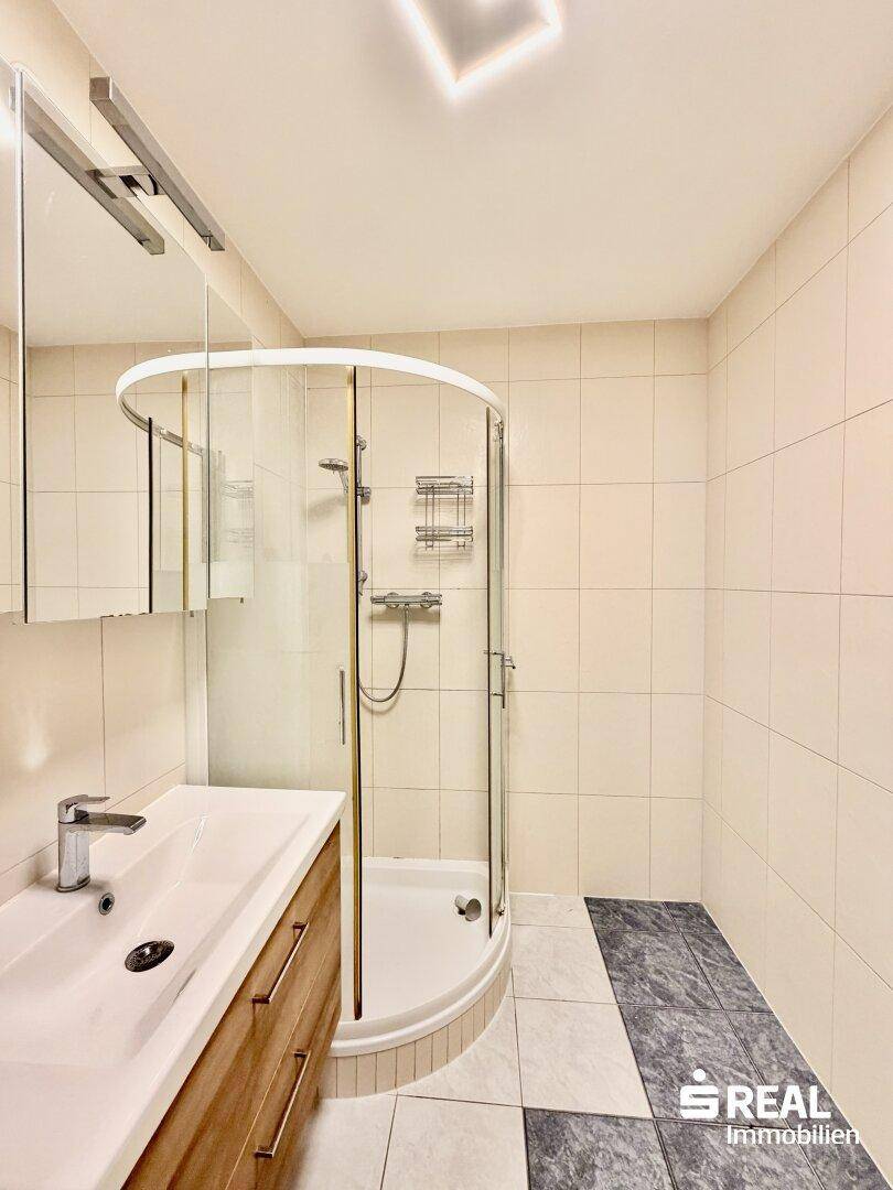 Helles Badezimmer mit Duschkabine, modernem Waschbecken und Spiegelschrank.