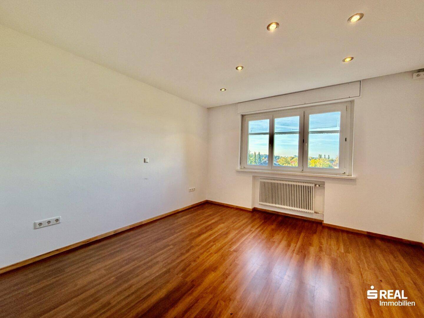 Helles Zimmer mit Holzboden, großem Fenster und Blick auf die Umgebung.