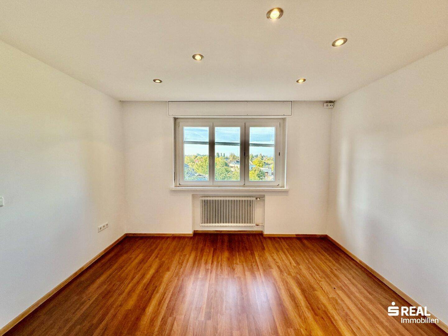 Geräumiges Zimmer mit Holzboden, Einbaustrahlern und Fenster mit Rollladen.