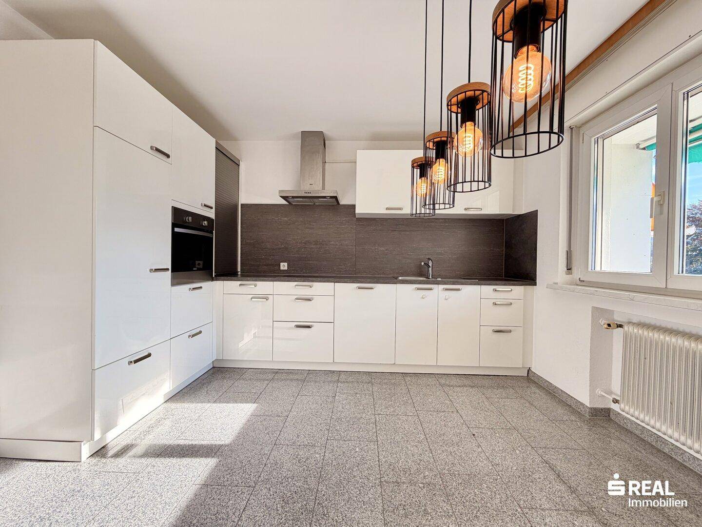 Moderne Küche mit weißen Hochglanzschränken, integrierten Geräten und dunkler Arbeitsplatte.