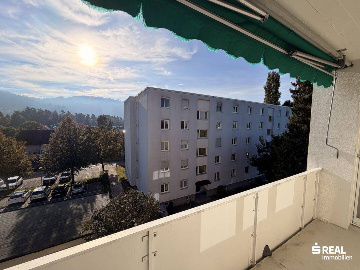 Balkon mit Markise und Blick auf die umliegende Wohngegend und grüne Hügel.