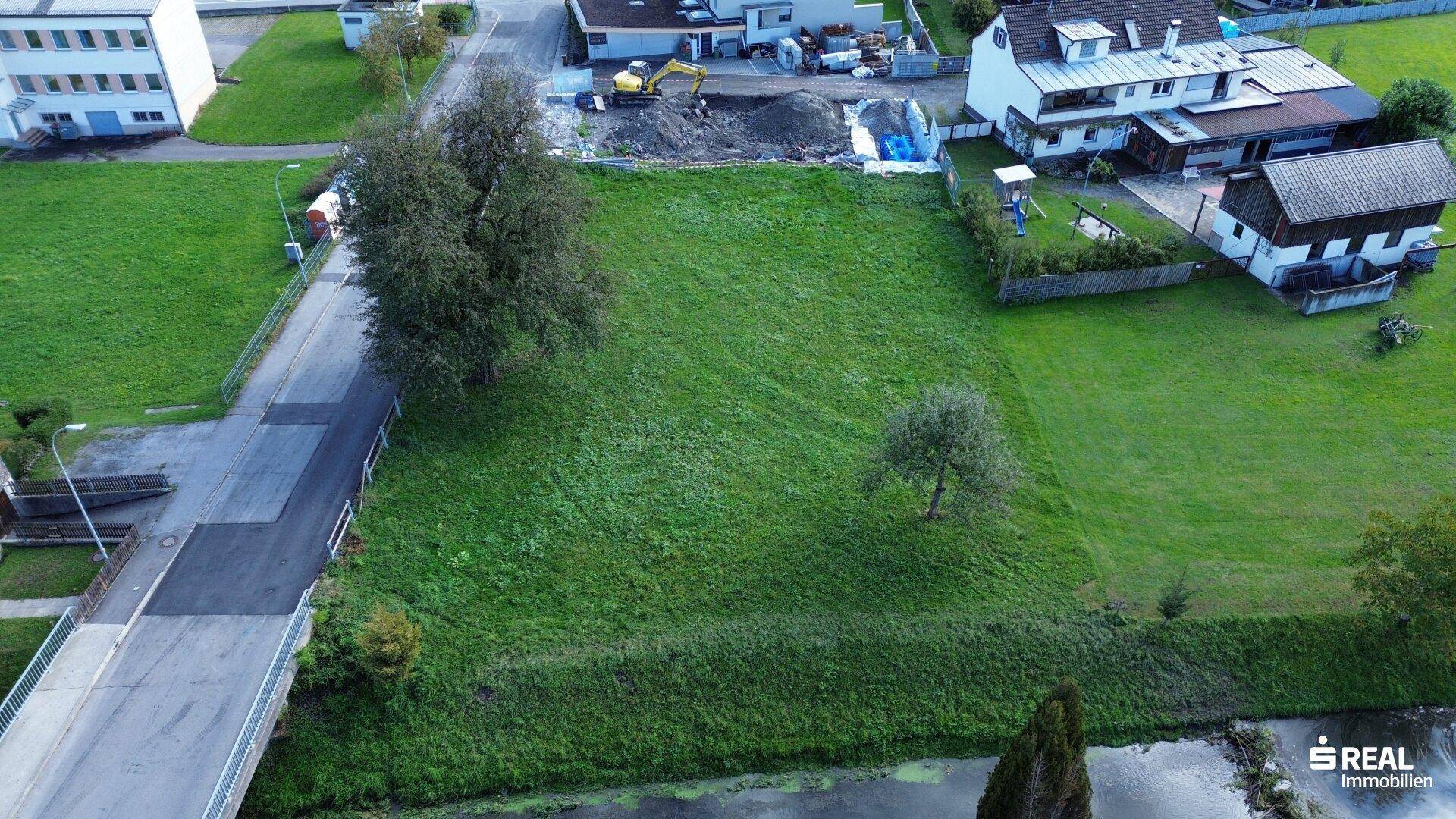 Übersichtliche Luftaufnahme des grünen Grundstücks mit Bachlauf, Brücke und angrenzenden Wohngebäuden.