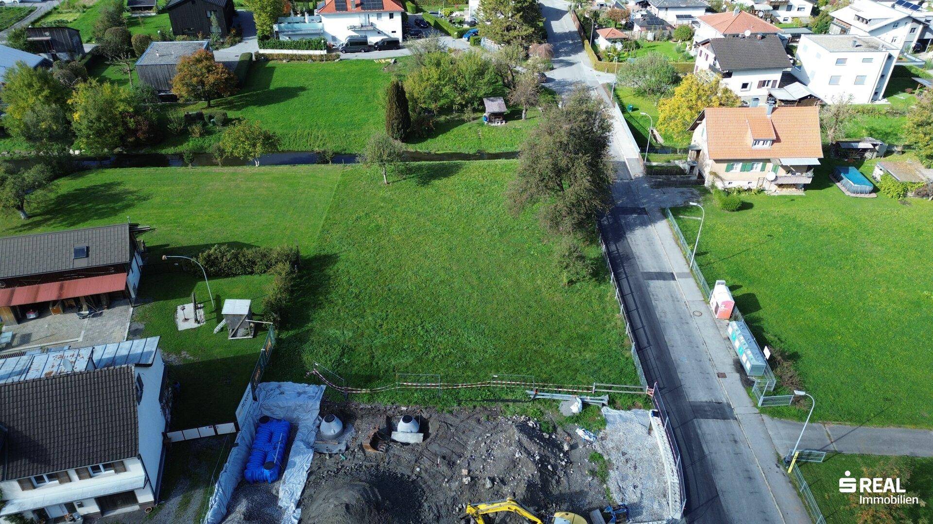 Luftaufnahme des Grundstücks mit angrenzender Straße, Bachlauf und umliegender Wohnbebauung.