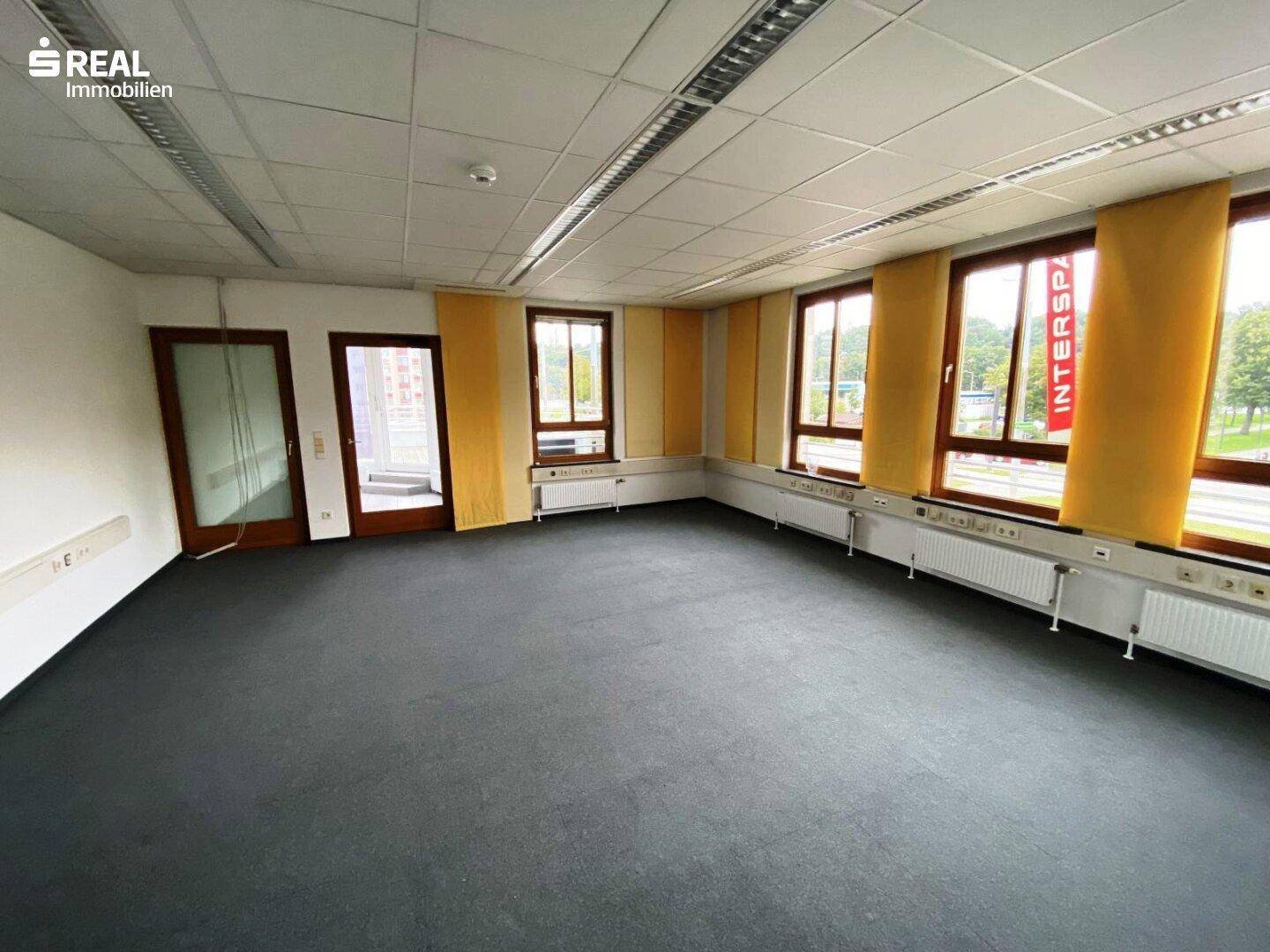 Großes Büro mit Teppichboden, vielen Fenstern und gelben Sichtschutzrollos.