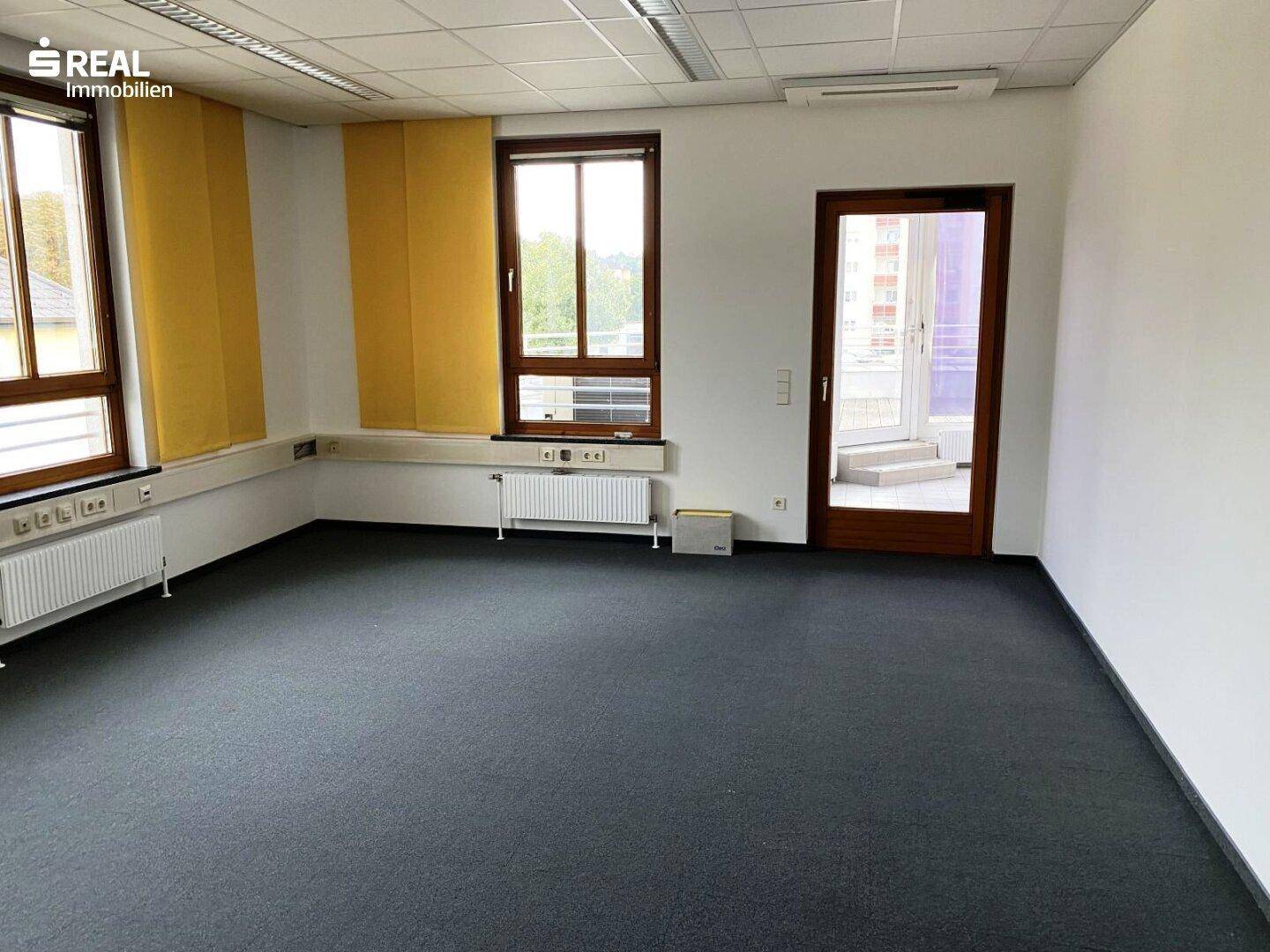 Helles Büro mit Teppichboden, großen Fenstern und Zugang zu einem weiteren Raum.