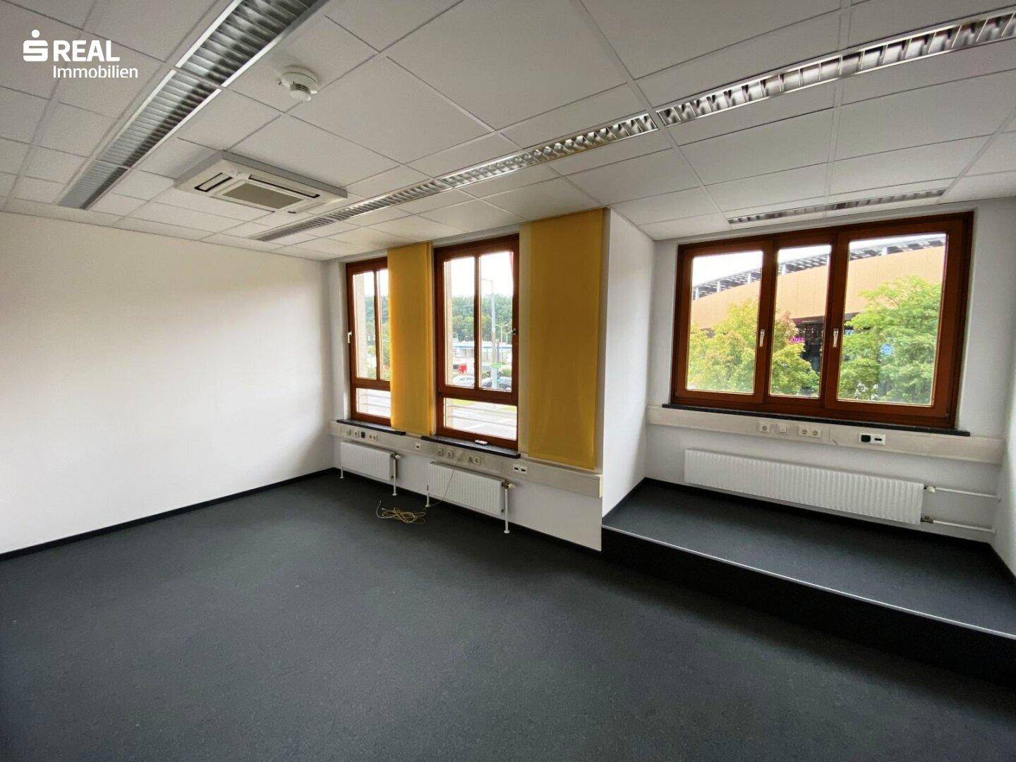 Modernes Büro mit Teppichboden, abgehängter Decke und Fenstern mit Blick ins Grüne.