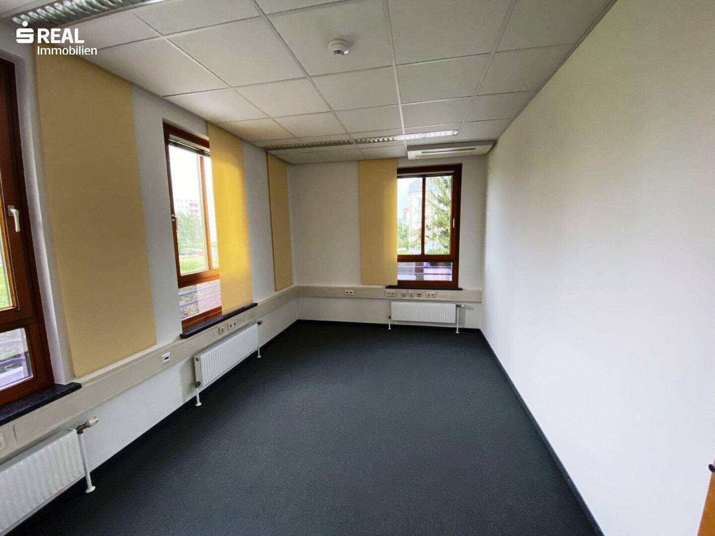 Helles Büro mit Teppichboden, weißen Wänden und Fenstern mit gelben Rollos.