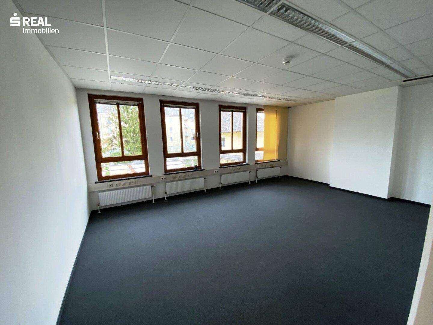 Großes, leeres Büro mit Teppichboden, weißen Wänden und einer Reihe von Fenstern.