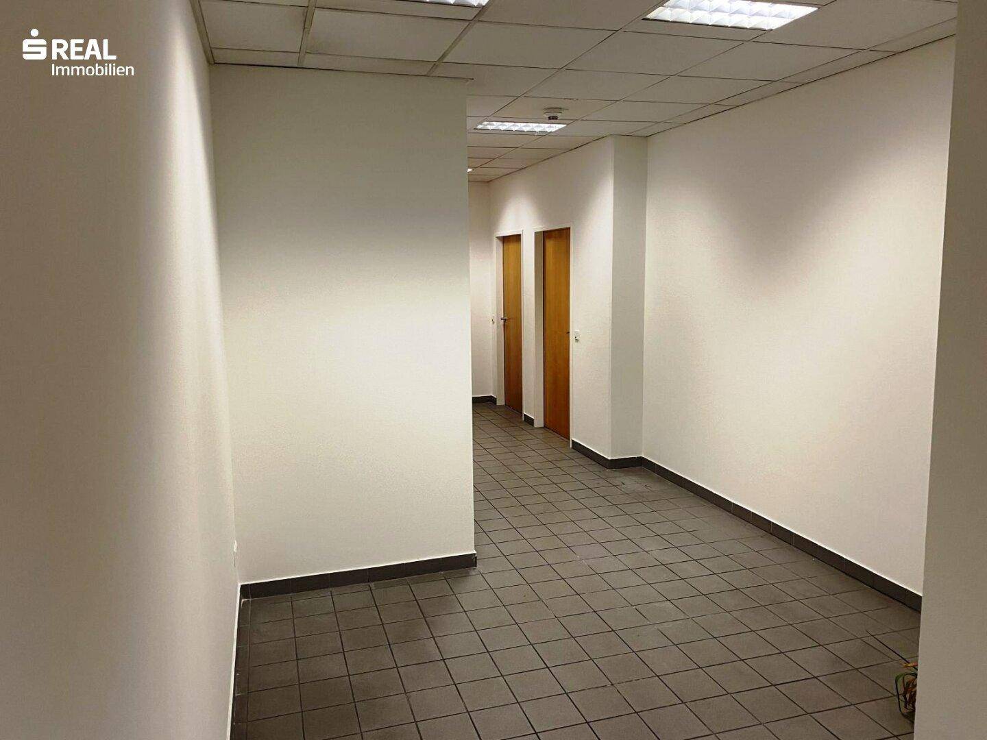 Langer Flur mit Fliesenboden, weißen Wänden und mehreren Holztüren.