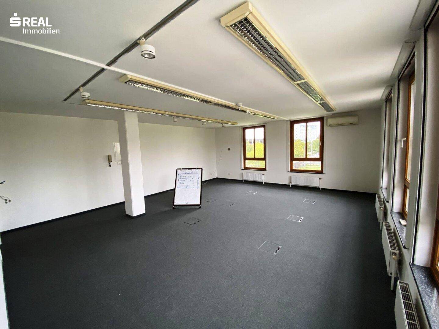 Großes Büro mit Teppichboden, vielen Fenstern und integrierten Bodentanks.