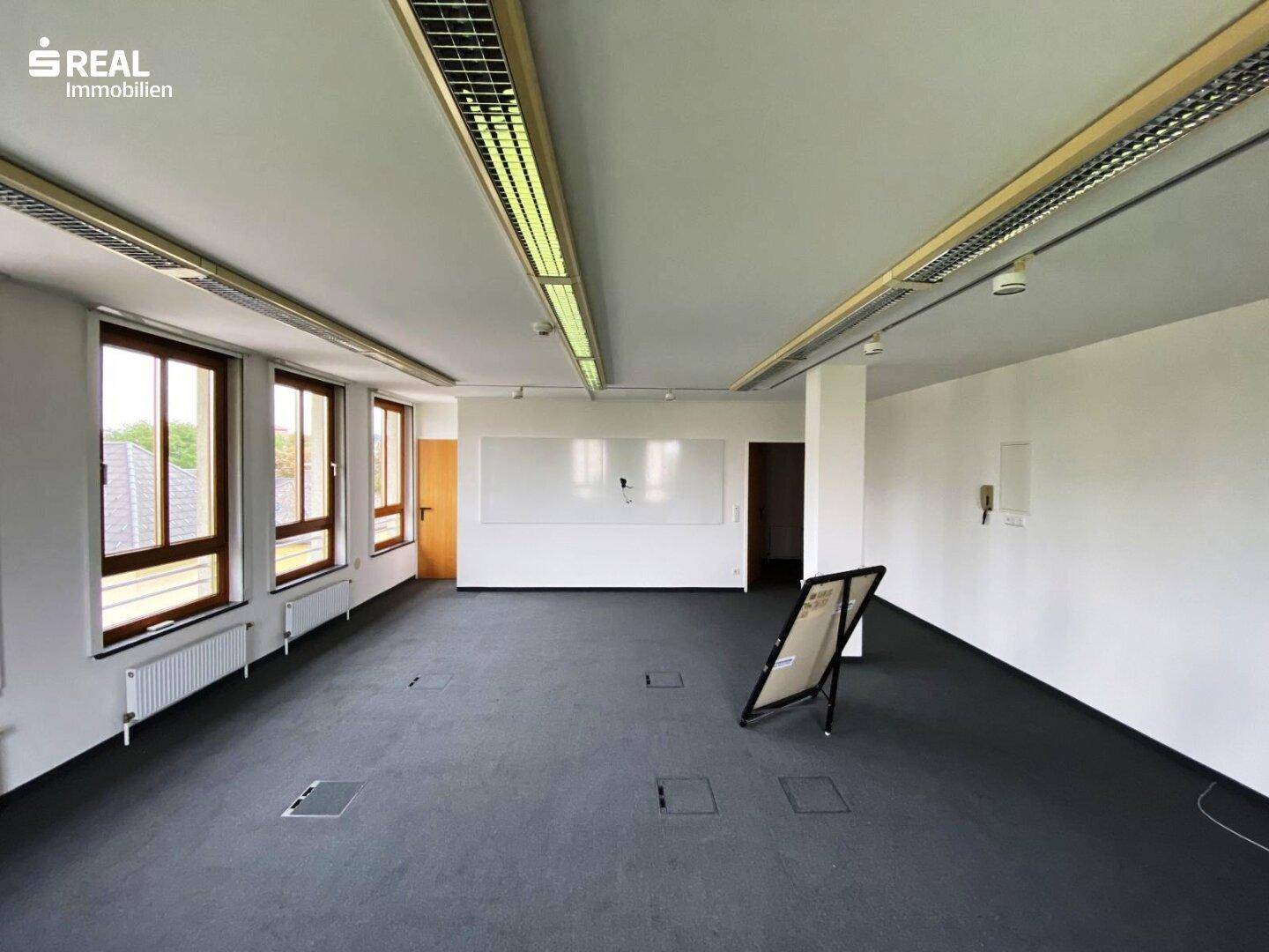 Geräumiges Büro mit Teppichboden, weißen Wänden und einer großen Whiteboard-Fläche.