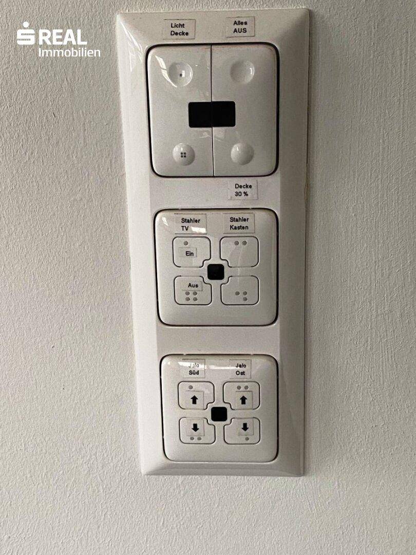 Modernes Bedienfeld für Licht, TV und Jalousien an einer weißen Wand.