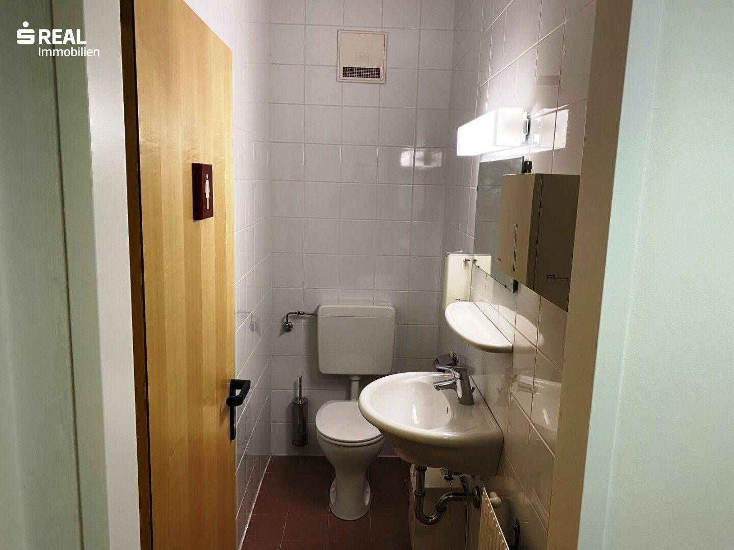 Kleiner Toilettenraum mit weißen Fliesen, Waschbecken und WC.