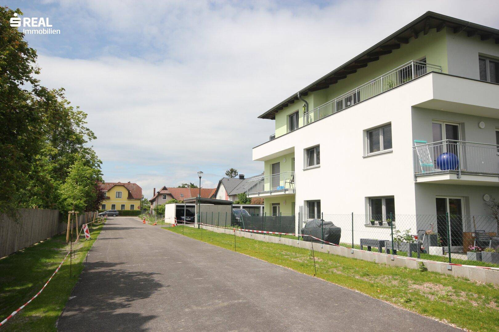 Blick auf die ruhige Wohnstraße und die moderne Fassade des Mehrfamilienhauses.