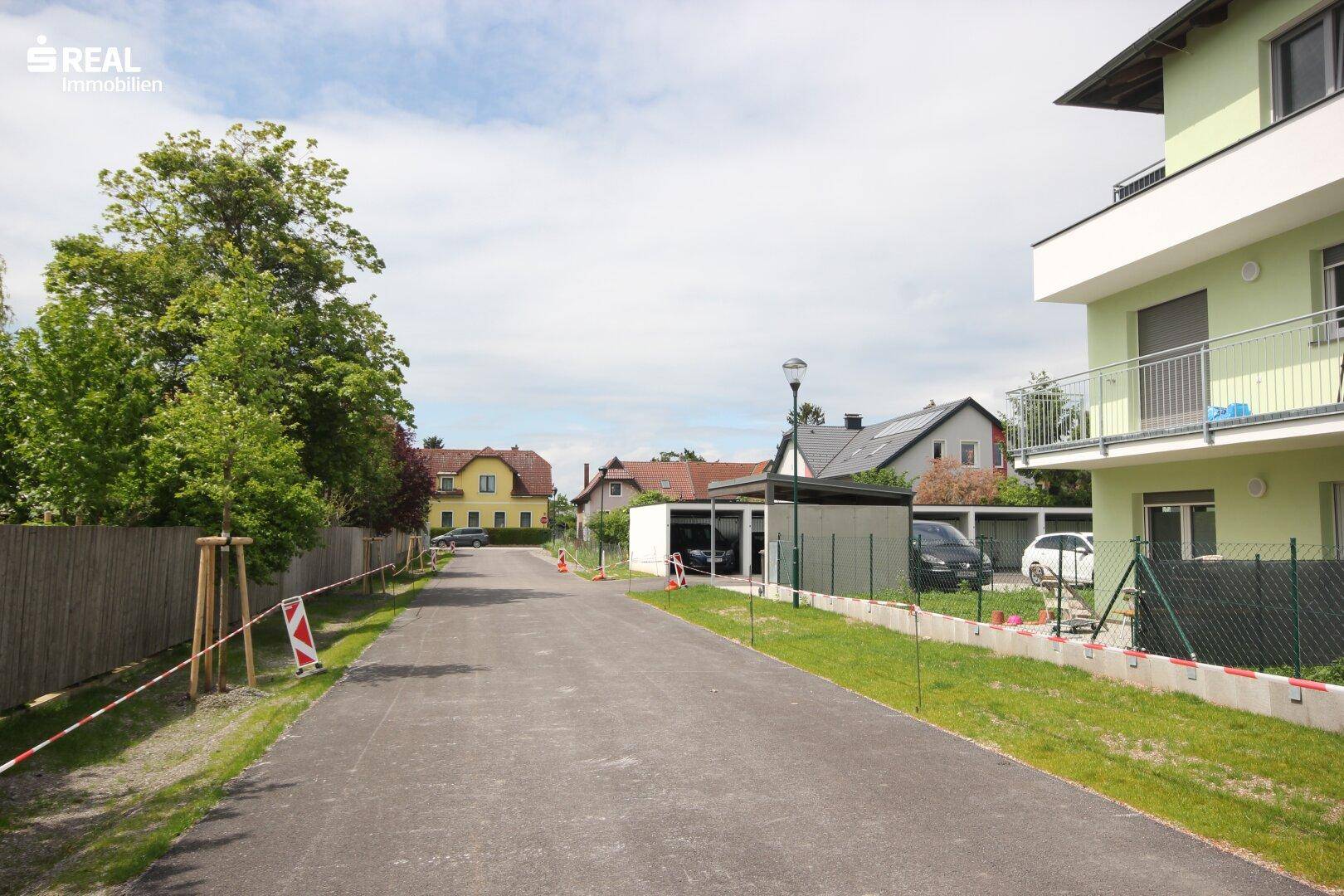 Ruhige Wohnstraße mit angrenzenden Häusern und viel Grün in ländlicher Umgebung.