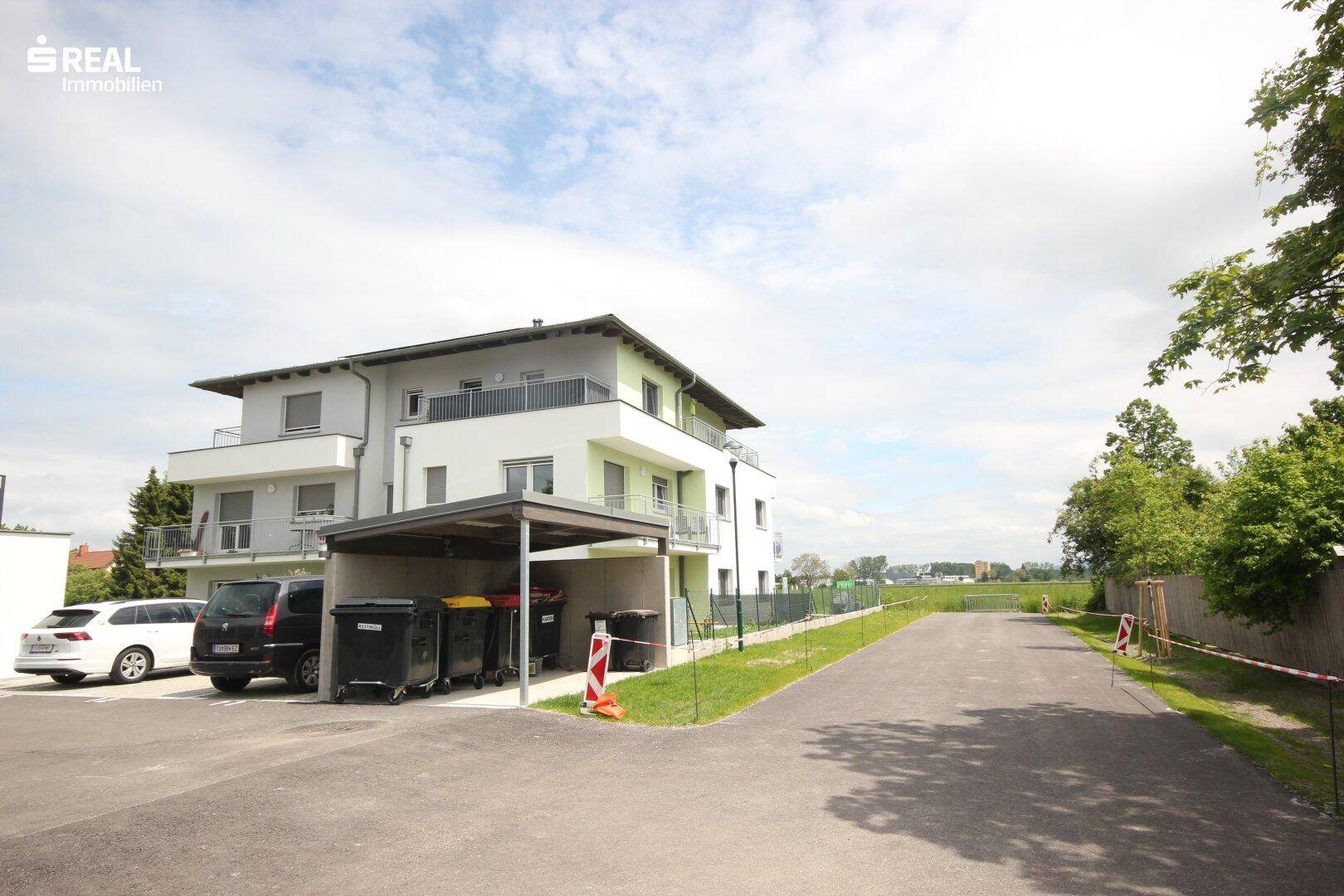 Rückansicht des modernen Gebäudes mit Carport und Mülltonnenbereich.