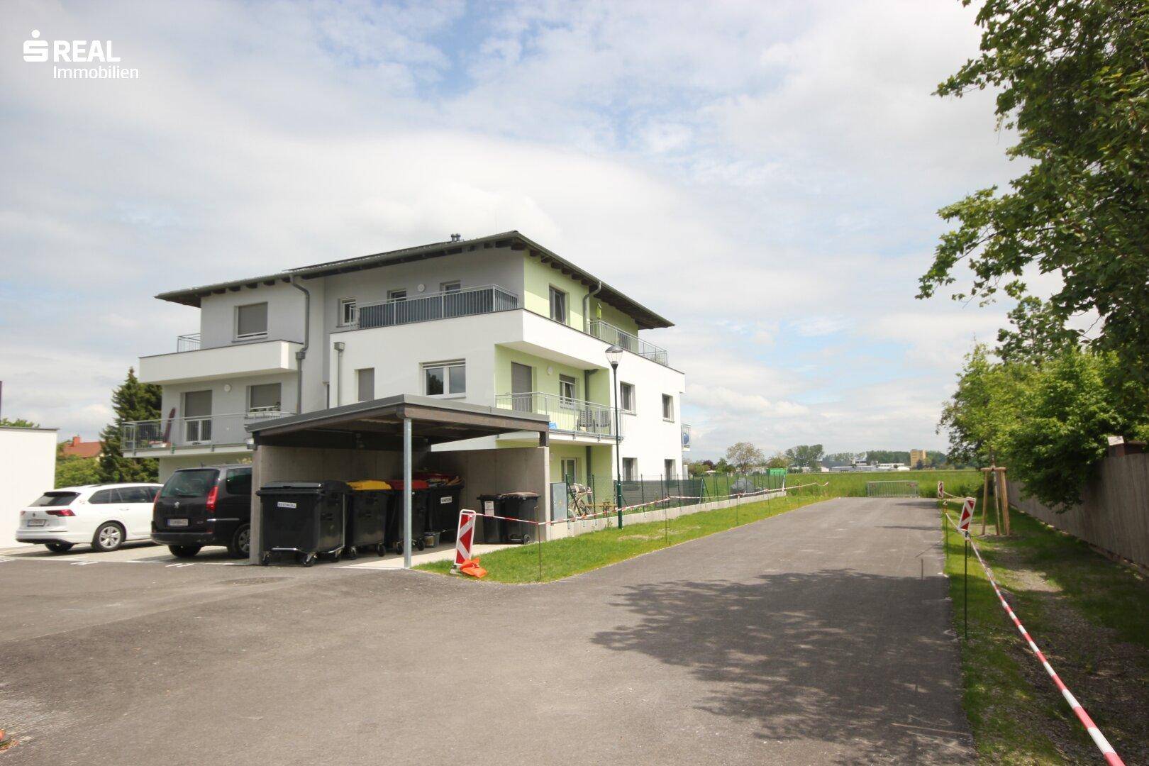 Ansicht des Mehrfamilienhauses mit überdachtem Parkplatz und angrenzender Straße.