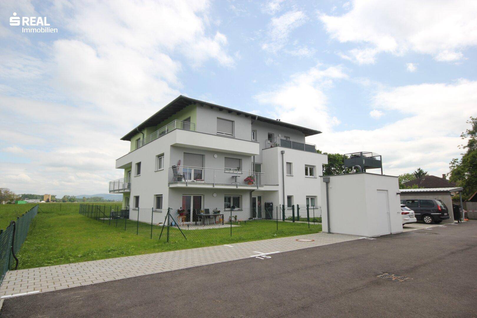 Modernes Wohnhaus mit Balkonen und Terrassen, angrenzend an eine weite Grünfläche.