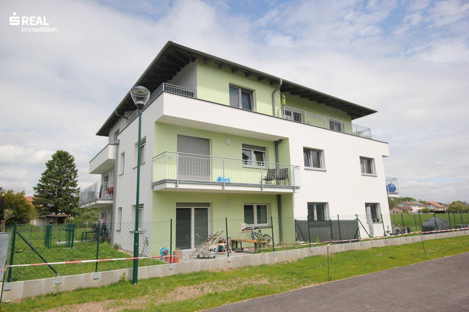 Modernes Wohnhaus mit Balkonen und einem kleinen, eingezäunten Gartenbereich.