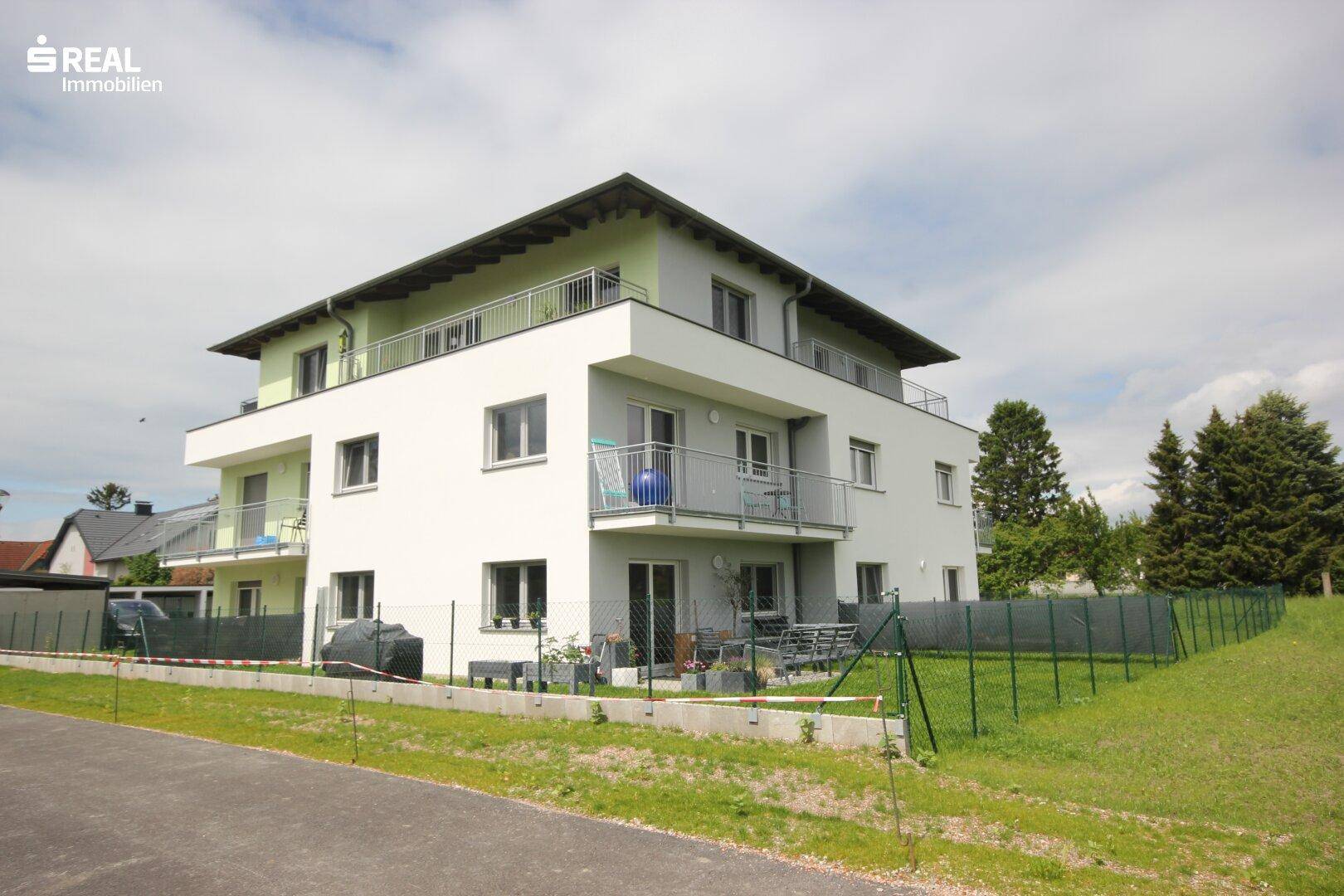 Modernes Mehrfamilienhaus mit weißer und grüner Fassade, umgeben von einer Grünfläche.