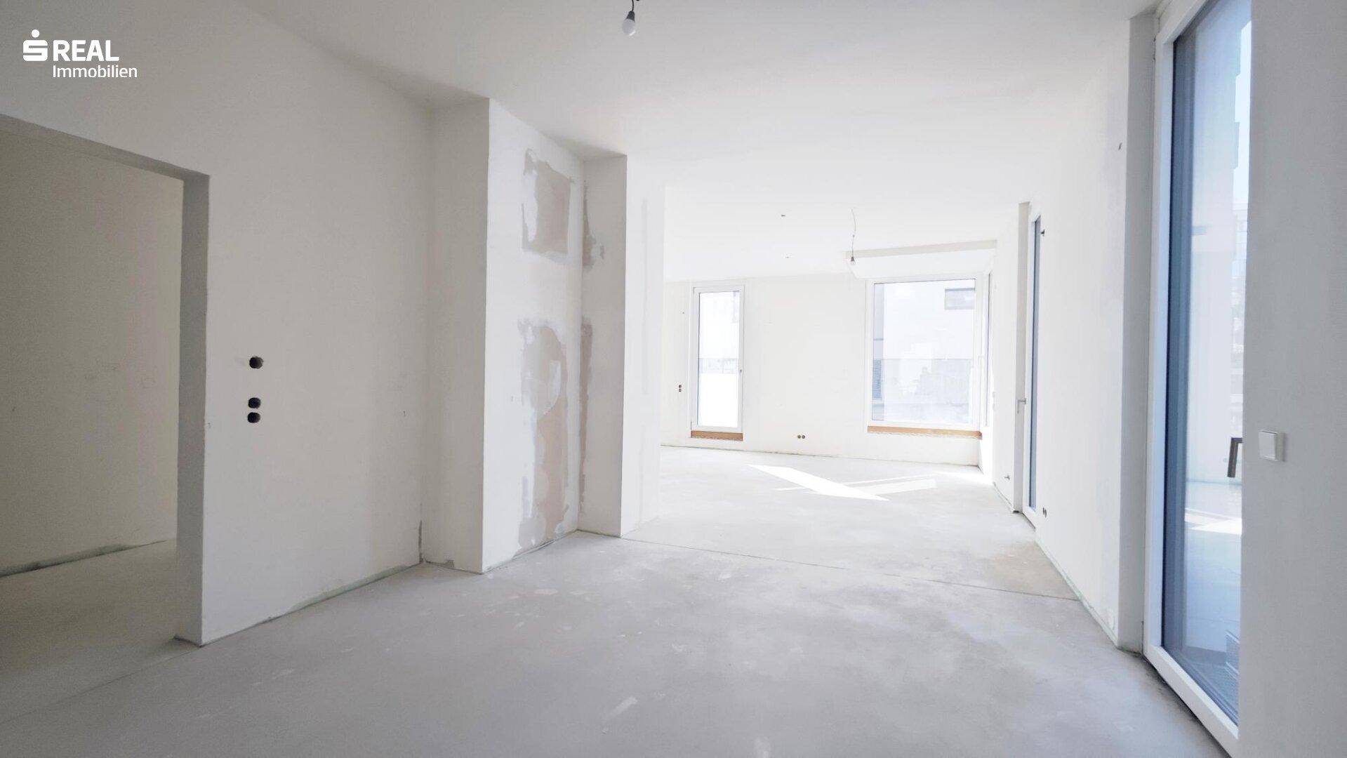 Geräumiger, unfertiger Innenraum mit viel Tageslicht durch große Fenster, bereit für die individuelle Gestaltung.