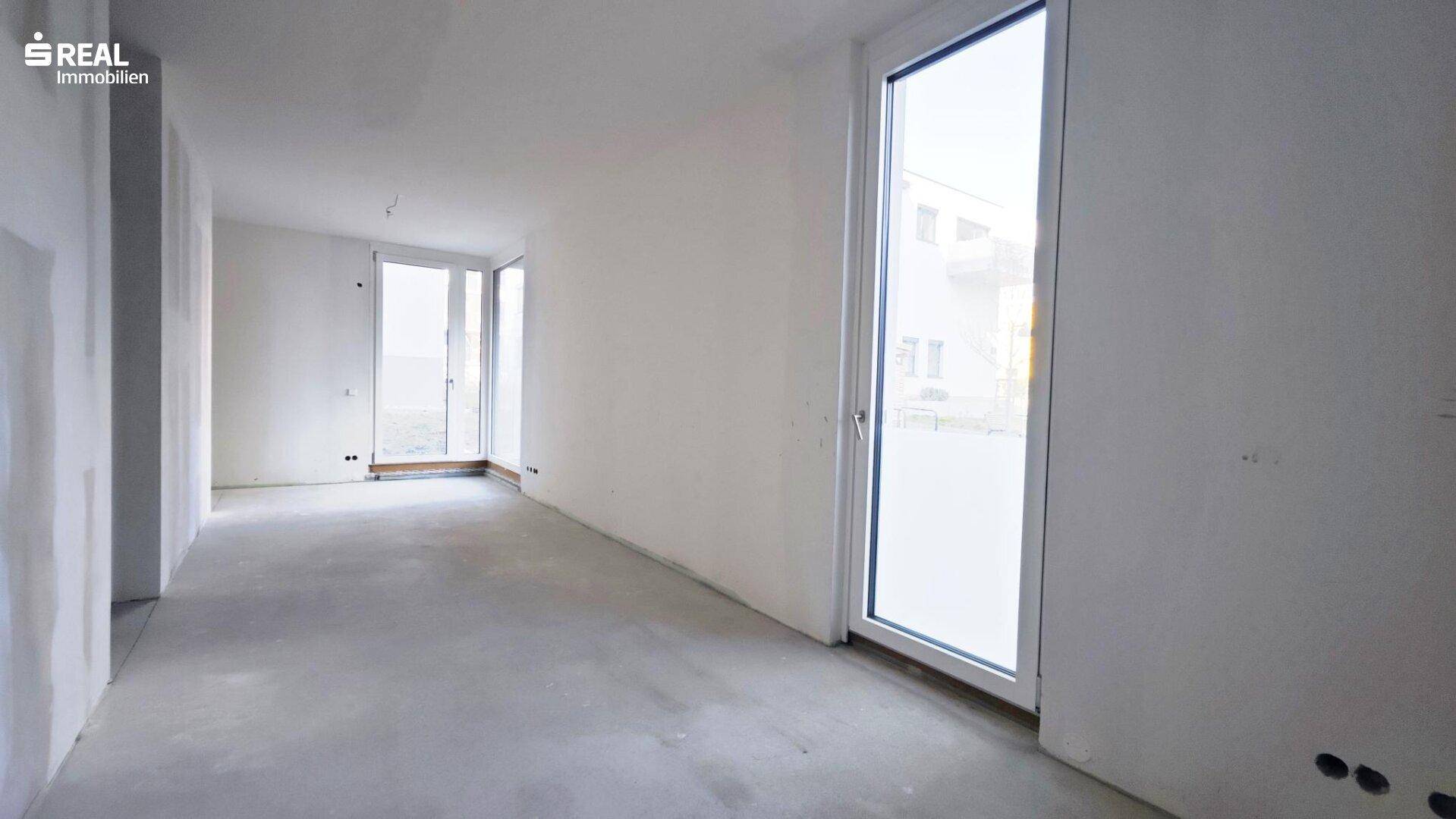 Heller, unfertiger Raum mit weißen Wänden und Betonboden, bereit für den weiteren Ausbau und die Gestaltung.