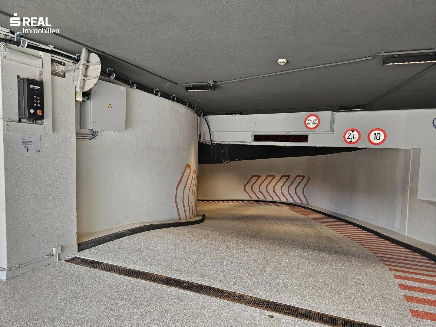 Geschwungene Zufahrtsrampe zu einer Tiefgarage mit Höhenbegrenzung und klaren Markierungen.