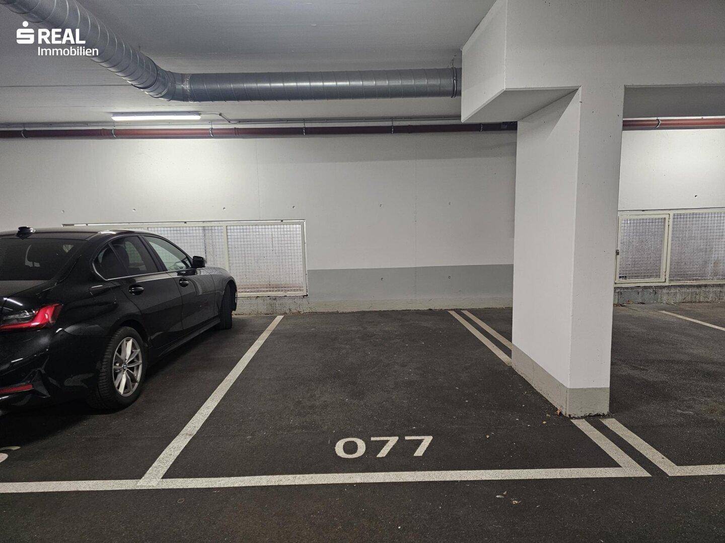 Ein freier Parkplatz in der Tiefgarage, gekennzeichnet mit der Nummer 077, neben einem geparkten Auto.